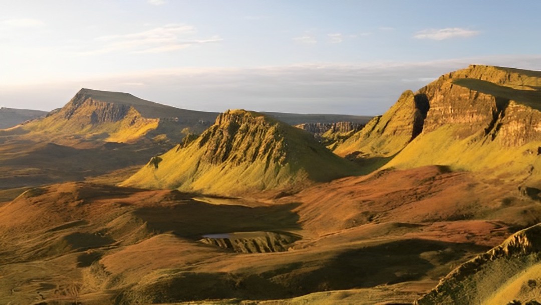 Golden light bathes the dramatic Quiraing landscape, showcasing the unique rock formations of Skye’s beauty
