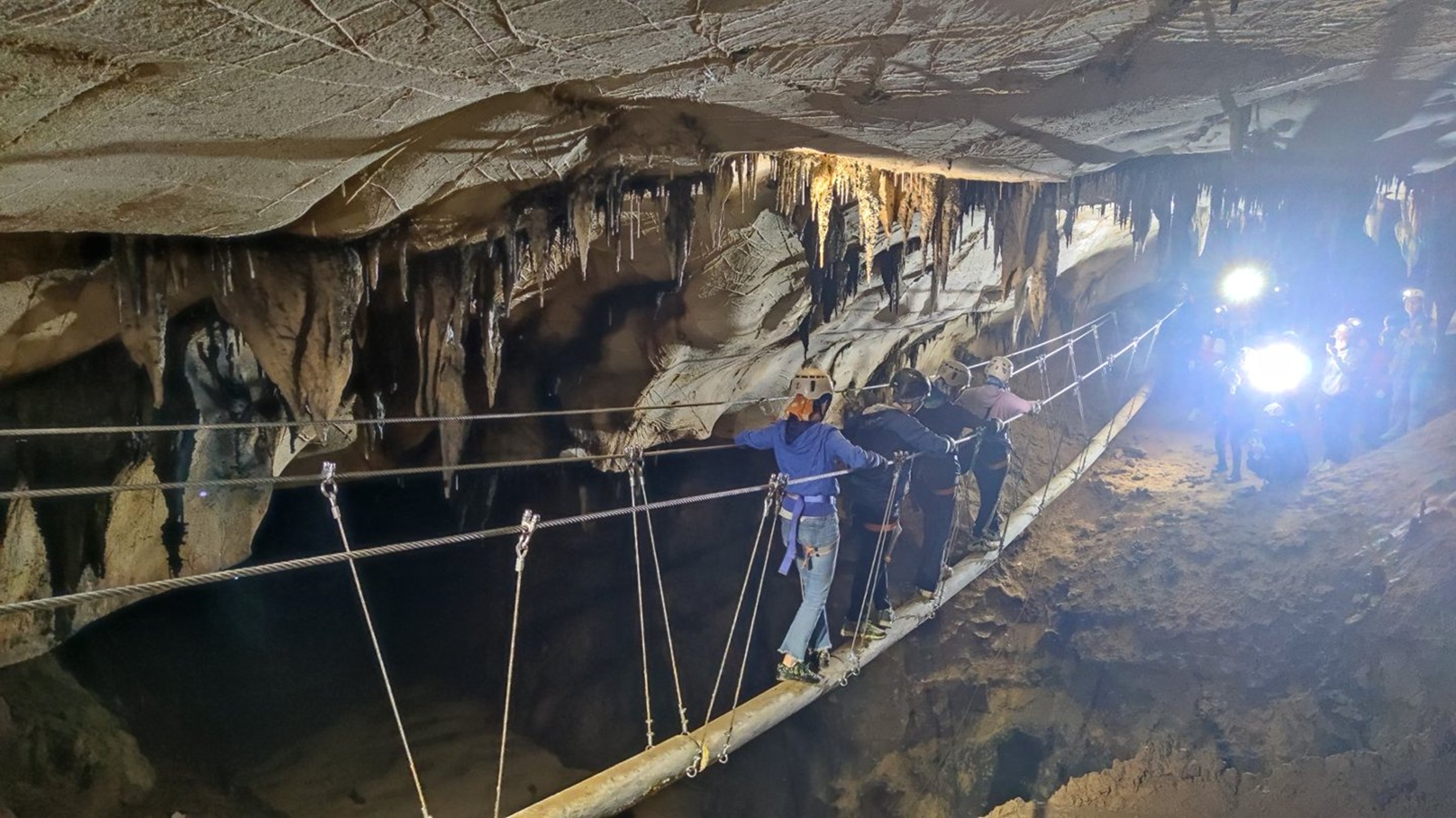 探險小隊在溶洞懸橋上列隊前行,頭燈與暖光刺破黑暗,鐘乳石垂掛如簾,腳下暗谷幽深,盡顯團隊協作的勇氣 探險小隊在溶洞懸橋上列隊前行,頭燈與暖光刺破黑暗,鐘乳石垂掛如簾,腳下暗谷幽深,盡顯團隊協作的勇氣