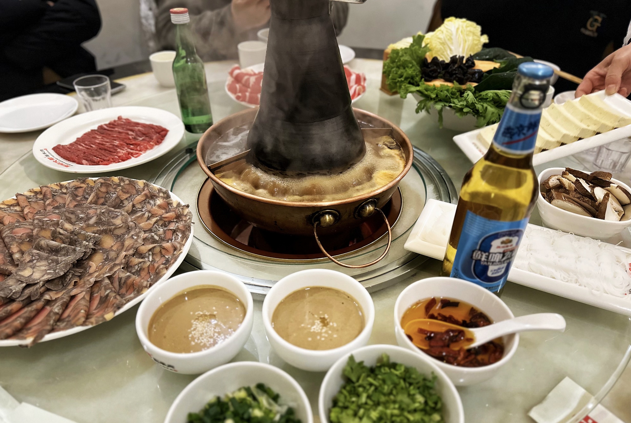 緊接著，一頭扎進那熱氣蒸騰、香氣四溢的火鍋世界，探尋北京的標誌性美食——涮羊肉火鍋。眼前古樸的銅鍋中間燒著通紅炭火，鍋底的湯在這熱力下持續穩定地翻滾，鍋中主要食材是那薄切得新鮮羊肉，紋理清晰。除了羊肉還有鮮嫩的牛肉、雞肉，以及琳琅滿目的新鮮蔬菜和菌類，任您隨心挑選。蘸料堪稱這美食體驗的點睛之筆。常見的蘸料以醇厚的腐乳與香濃的芝麻醬精心調和而成，若是您鍾情辣味，只需添上些許辣椒油，瞬間便能激發出別樣的熱辣風情。而冰爽沁涼的啤酒絕對是絕佳的飲品搭配，一口酒一口涮肉，讓味蕾在冰火交融間盡享極致歡愉 。