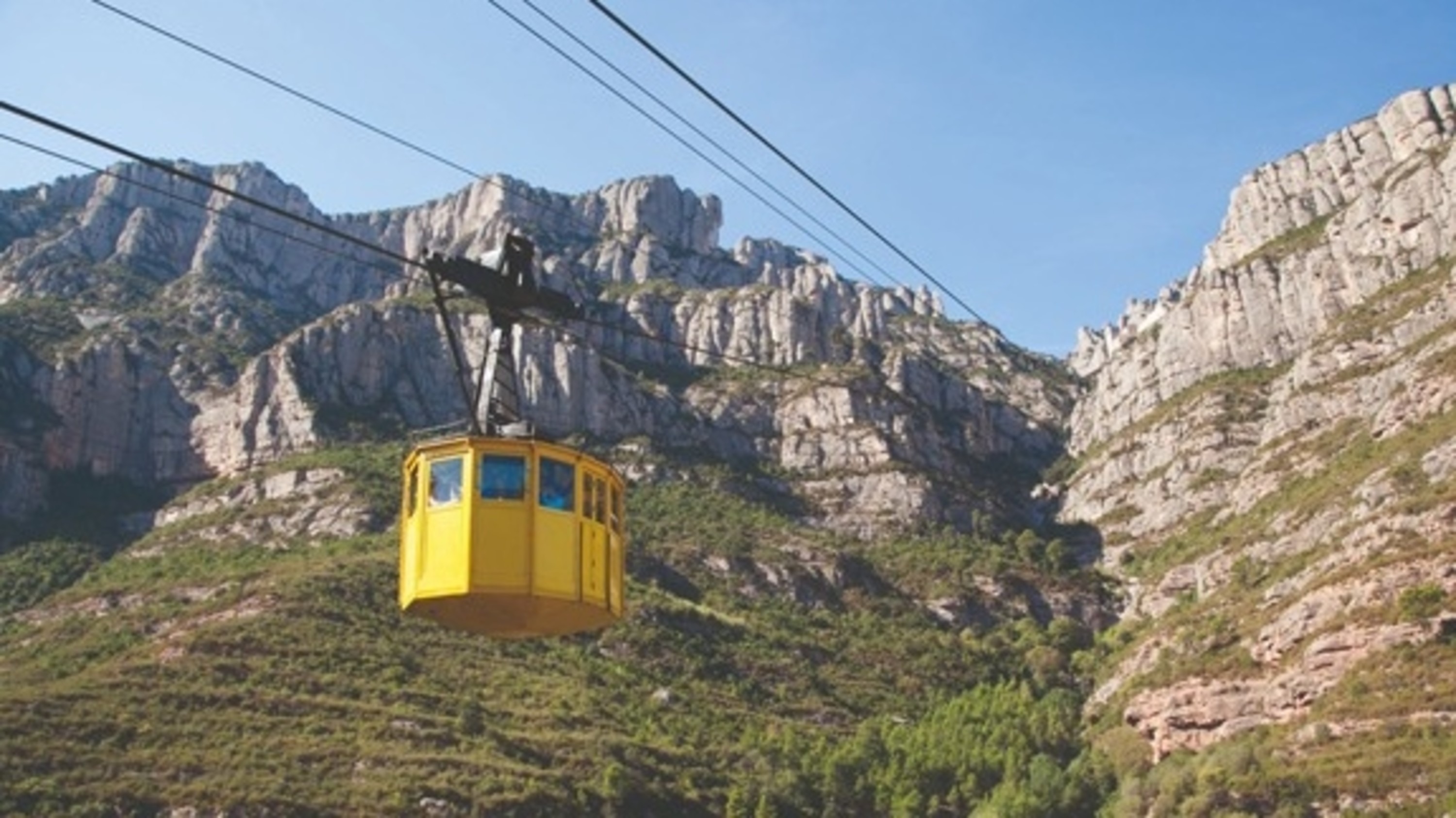 The iconic yellow Aeri cable car ascends toward Montserrat, suspended above the valley