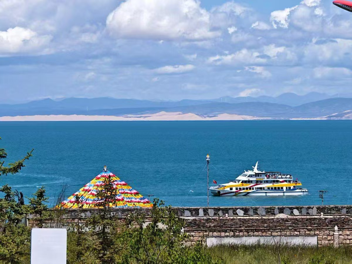 遼闊湛藍青海湖視野開闊,遠景沙丘淺淡,岸邊五彩經幡藏味十足。鮮亮觀光遊船行駛湖面,載滿遊客,石牆綠植點綴岸邊,藍天白雲相伴,融合湖泊風光與環湖遊玩氣息 遼闊湛藍青海湖視野開闊,遠景沙丘淺淡,岸邊五彩經幡藏味十足。鮮亮觀光遊船行駛湖面,載滿遊客,石牆綠植點綴岸邊,藍天白雲相伴,融合湖泊風光與環湖遊玩氣息
