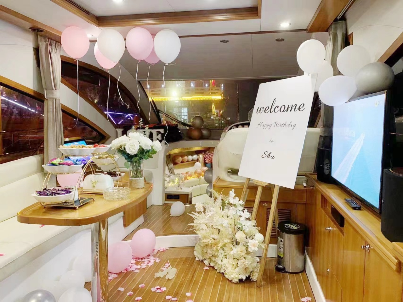 Warm yellow light spilled across the yacht's wooden floors, pink and white balloons hung in the air, and petals and floral arrangements spread along the welcome sign.