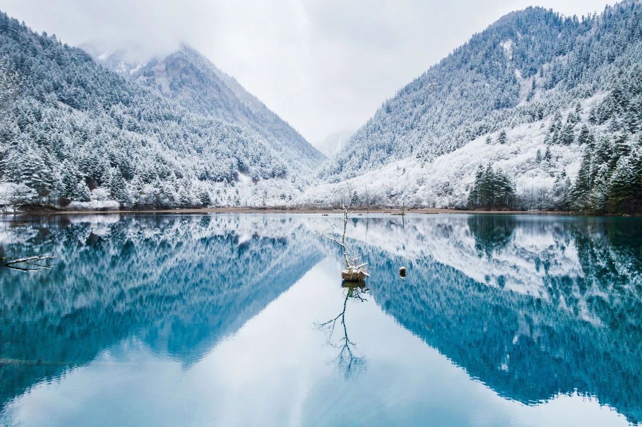 雲霧輕籠天際，湖水凝著寶石藍，兩岸山林裹滿雪絨，白與藍在鏡面裡織成素淨的畫，連風都輕得不敢打破這方靜謐。