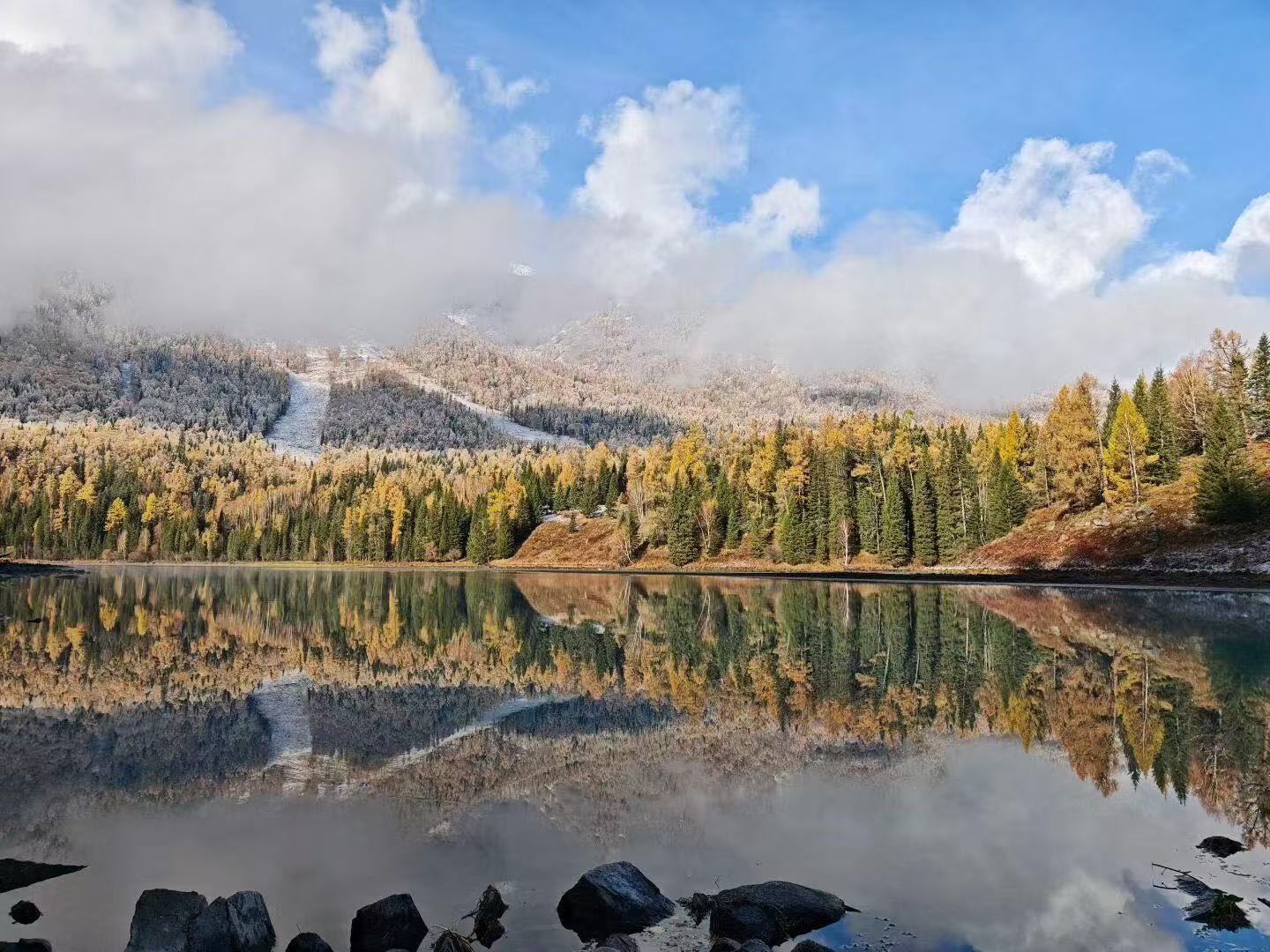 澄澈湖面如鏡面，完整復刻山林雪峰。彩林層次豐富，流雲漫過山巔，水天一體，靜謐治癒，宛若天然油畫