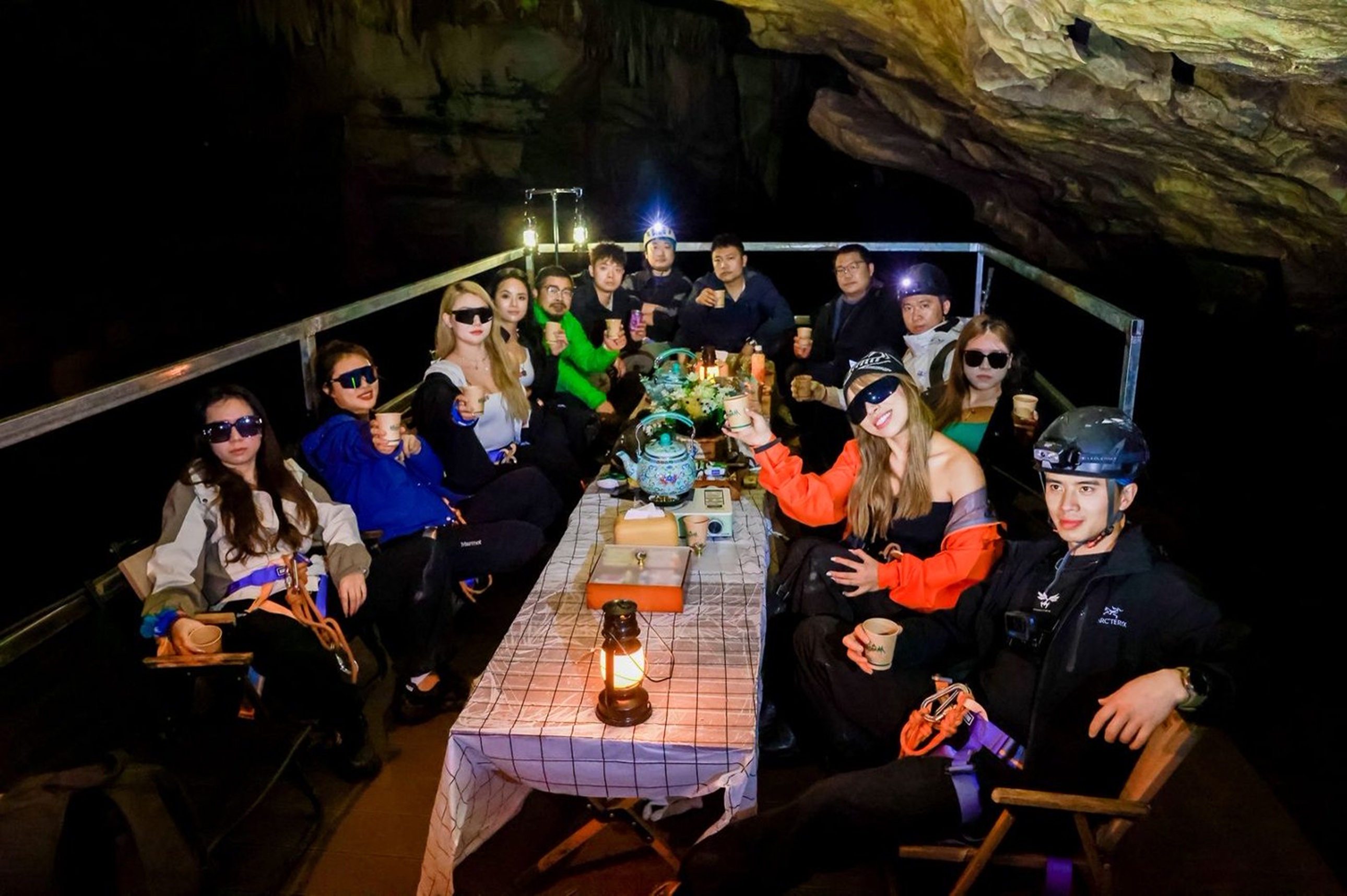 溶洞餐廳裡,眾人圍坐長桌舉杯,煤油燈與頭燈暖光交織,巖壁作背景,是探險後野奢又熱鬧的歡聚時刻 溶洞餐廳裡,眾人圍坐長桌舉杯,煤油燈與頭燈暖光交織,巖壁作背景,是探險後野奢又熱鬧的歡聚時刻