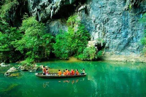 洞天仙境：遊船穿越200米溶洞水道，洞頂兩個通天穿孔灑下天光，在幽暗的洞廳中形成神秘光柱。光影與水霧交織，鐘乳石在彩燈映照下絢麗斑斕，水中倒影如夢似幻。