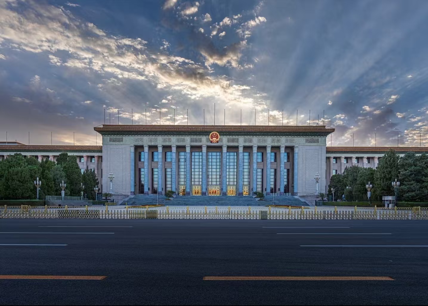 人民大會堂在晴空下莊重巍峨，淺灰石質立面搭配十二根巨柱，國徽高懸，紅旗獵獵，盡顯大國氣象與莊嚴氣度