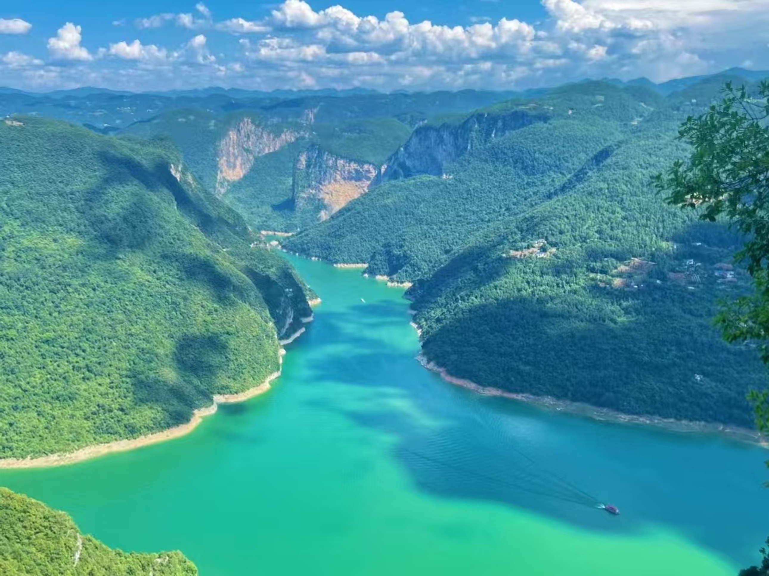 晴空下，青綠江面繞著翠嶺蜿蜒，遊船劃出波紋，山巒層疊如黛，是峽谷間的澄澈與壯闊