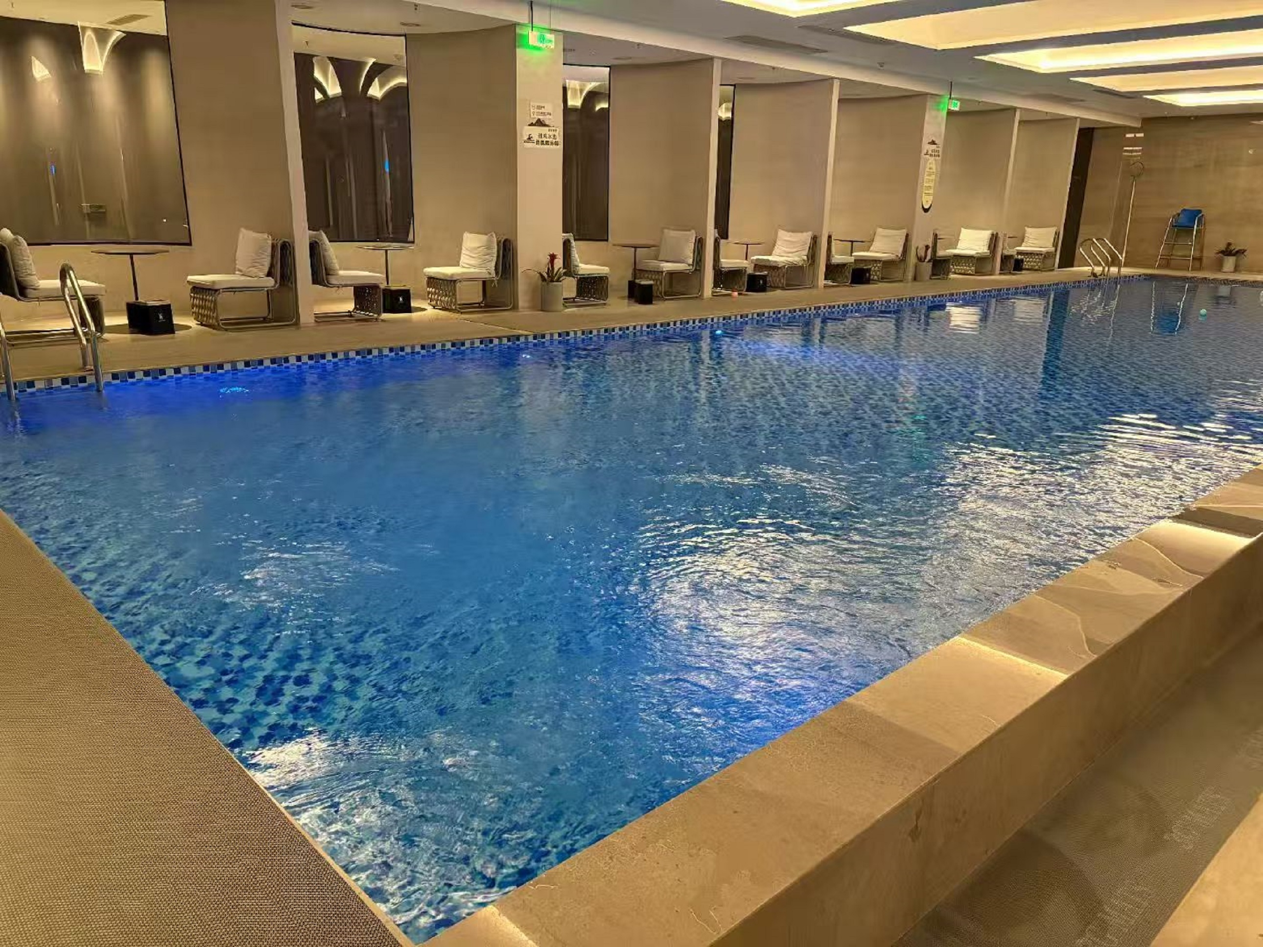 室內泳池的水湛藍清澈,池邊整齊排列著帶白色靠墊的休閒椅,牆面的鏡子和燈光讓空間顯得寬敞明亮,在這裡可以暢快游泳,也能在遊累後躺在椅上休息 室內泳池的水湛藍清澈,池邊整齊排列著帶白色靠墊的休閒椅,牆面的鏡子和燈光讓空間顯得寬敞明亮,在這裡可以暢快游泳,也能在遊累後躺在椅上休息