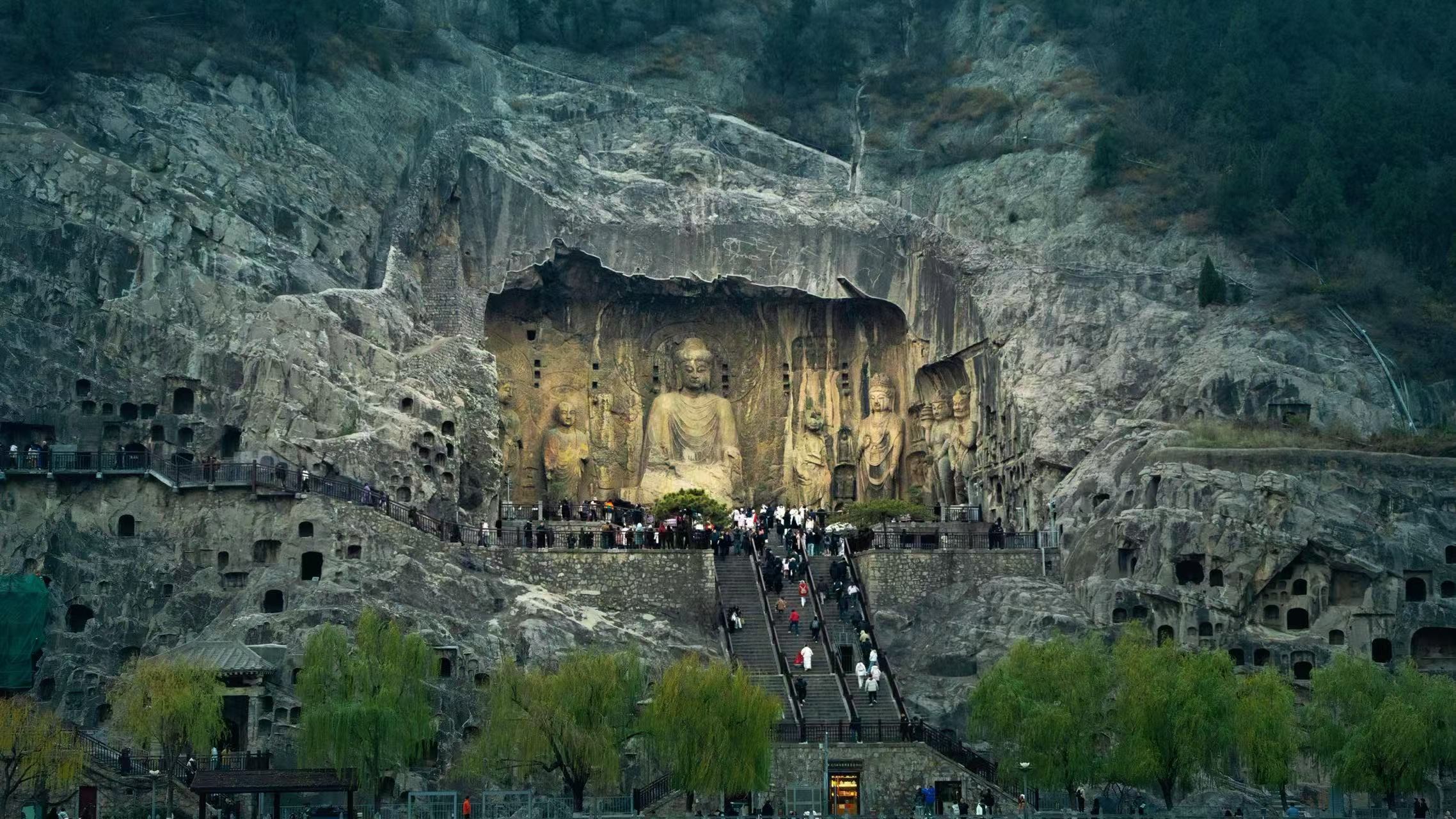 奉先窟全景:巨大的盧舍那大佛端坐於崖壁中央,兩側菩薩、弟子、天王造像依次排列,與陡峭的石灰岩山體融為一體。石階上游客絡繹不絕,在宏偉的石刻群前更顯渺小,直觀展現了 “石刻藝術最高峰” 的震撼氣勢 奉先窟全景:巨大的盧舍那大佛端坐於崖壁中央,兩側菩薩、弟子、天王造像依次排列,與陡峭的石灰岩山體融為一體。石階上游客絡繹不絕,在宏偉的石刻群前更顯渺小,直觀展現了 “石刻藝術最高峰” 的震撼氣勢
