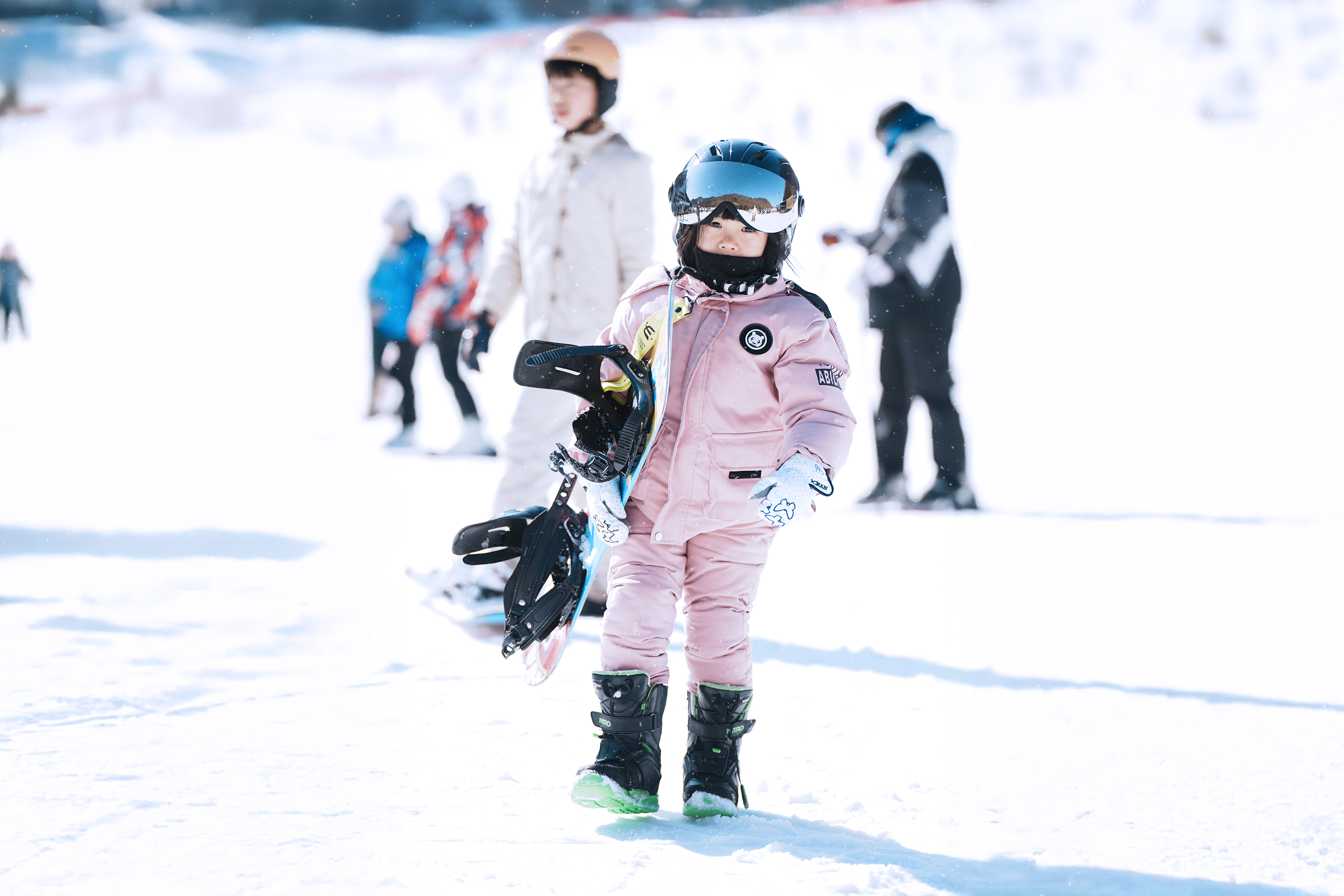 一位年輕的滑雪者在雪地上自信地邁出步伐，在一個充滿陽光和家庭氛圍的環境中享受學習的樂趣。