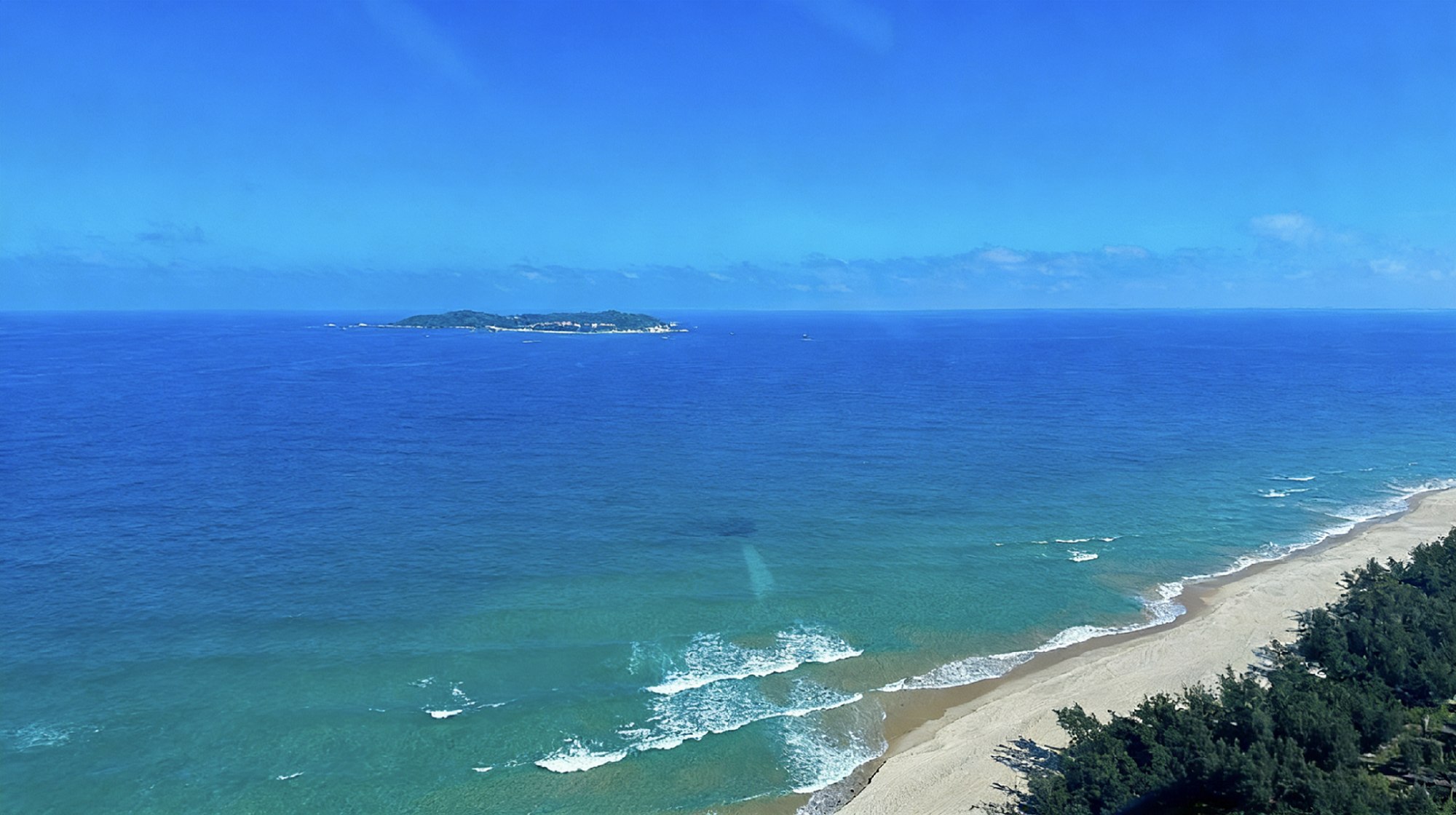 極目處，蜈支洲島縮成海面上的一抹綠，近處的沙灘與浪濤織成漸變藍的絨毯。風把雲絮吹得很薄