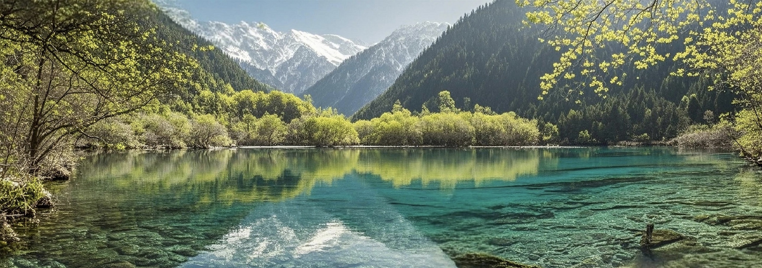 遠處雪山巍峨矗立，岸邊新綠的林木與嫩黃的枝椏交相輝映，春日的生機在湖光山色間肆意流淌