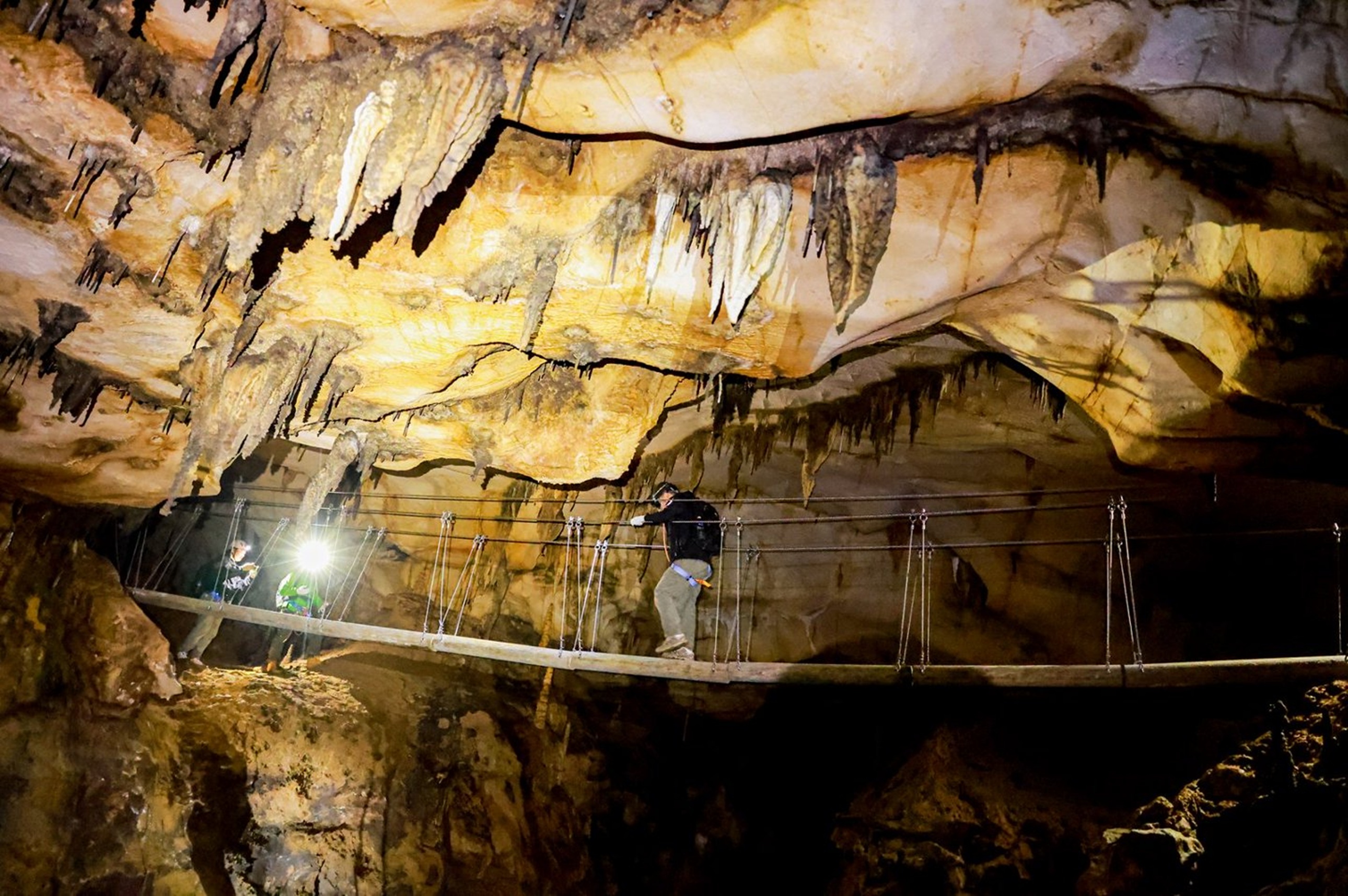 探險者在溶洞高空懸橋上穩步前行,巖壁鐘乳石垂掛如林,腳下是幽深暗谷,每一步都考驗著勇氣與平衡感 探險者在溶洞高空懸橋上穩步前行,巖壁鐘乳石垂掛如林,腳下是幽深暗谷,每一步都考驗著勇氣與平衡感