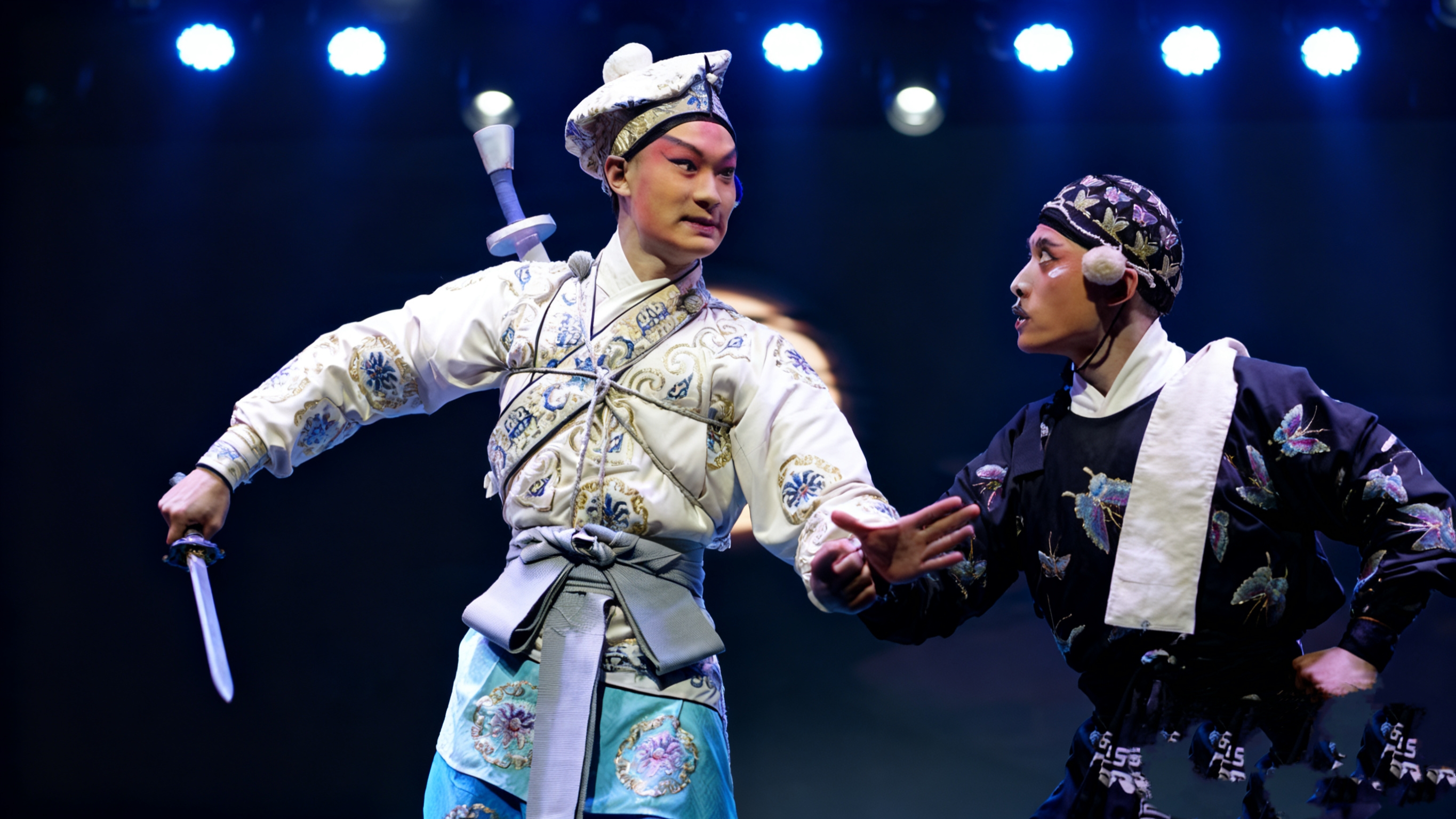 兩位京劇演員的互動充滿戲劇張力。上方的藍色燈光為場景增添了一絲冷峻感,將京劇武戲的魅力展現得淋漓盡致 兩位京劇演員的互動充滿戲劇張力。上方的藍色燈光為場景增添了一絲冷峻感,將京劇武戲的魅力展現得淋漓盡致