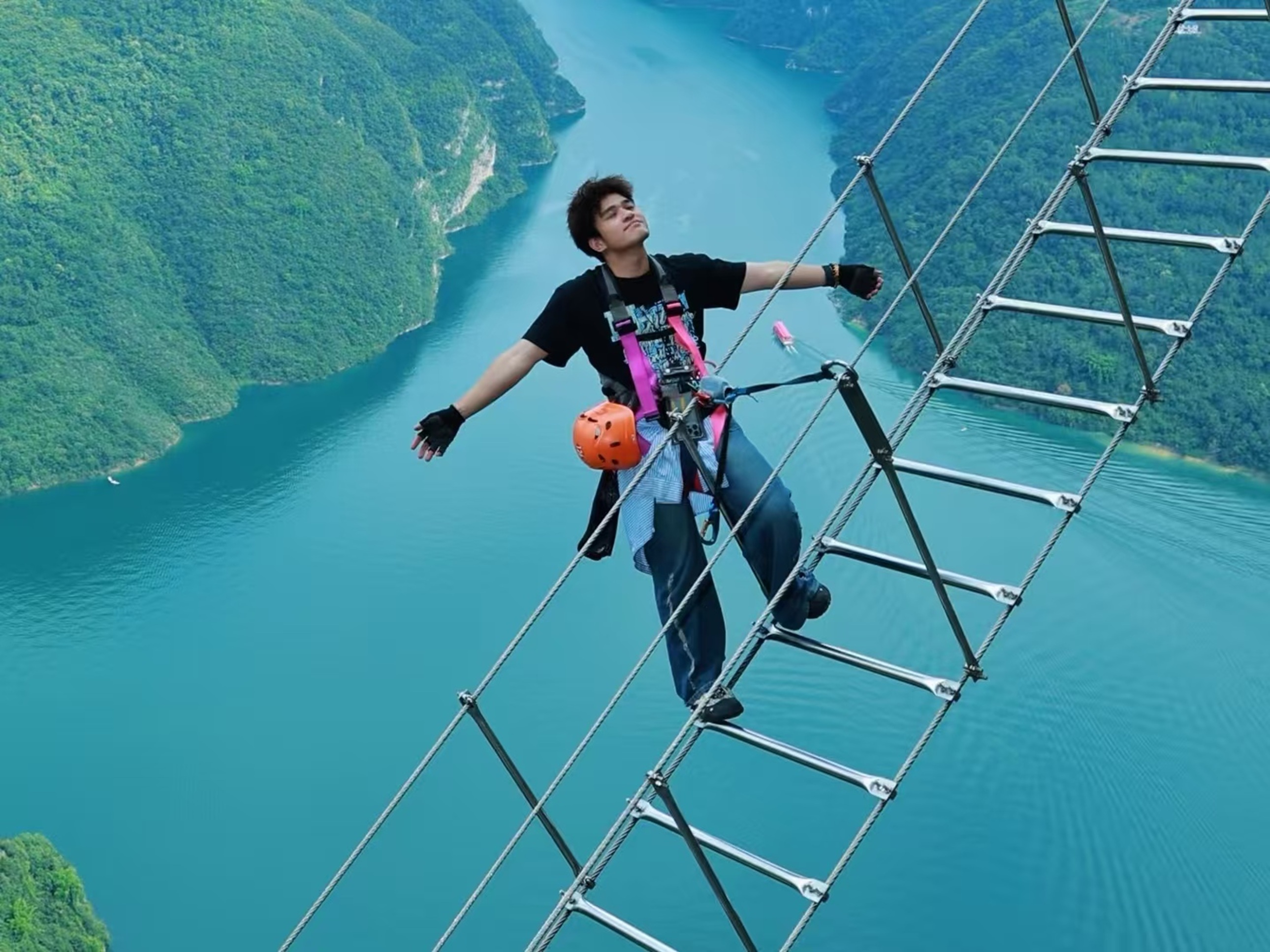 黑衣男子展臂立於高空梯，粉紫裝備襯著碧江翠嶺，姿態鬆弛，把高空挑戰變成了與山河的浪漫同框