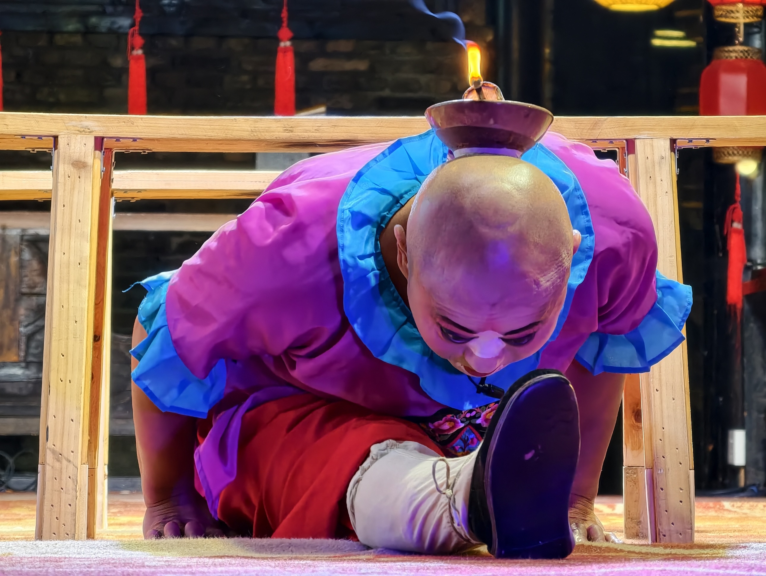 丑角演員身著色彩豔麗的戲服，頭頂燃著燈火的碗具，身體柔韌地做出高難度動作，在傳統戲曲的佈景前，將詼諧與精湛技藝融合，演繹出令人稱奇的表演瞬間