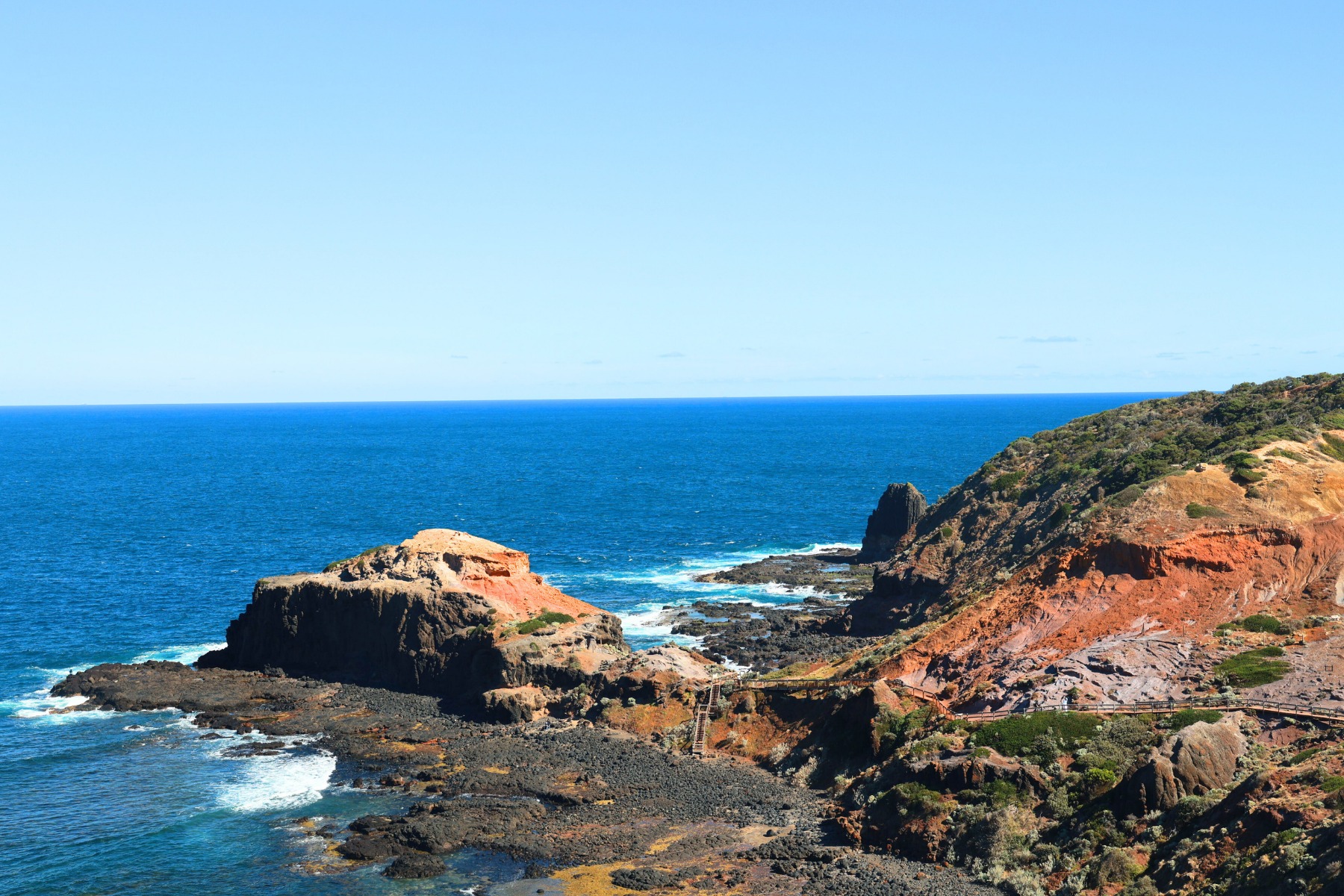 Walk the clifftop boardwalk to the lighthouse with crashing waves below.