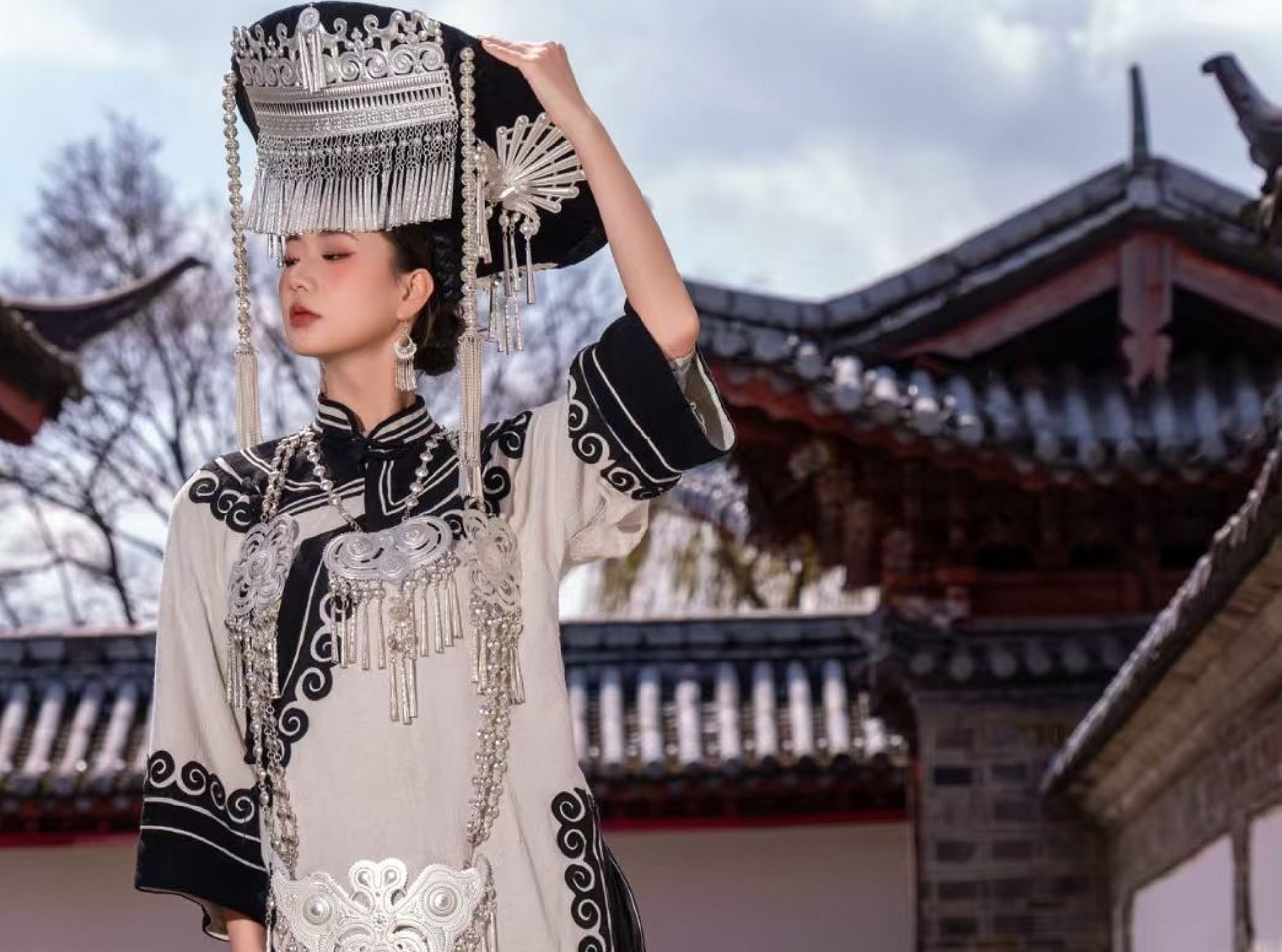 青瓦飛簷的古建旁，女子抬手輕扶頭頂的銀冠，白衫上的黑紋如墨韻流轉