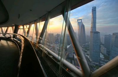 清晨時分，透過玻璃幕牆可看到上海中心大廈、環球金融中心等摩天大樓在晨光中若隱若現，天空呈現出漸變的橙黃色