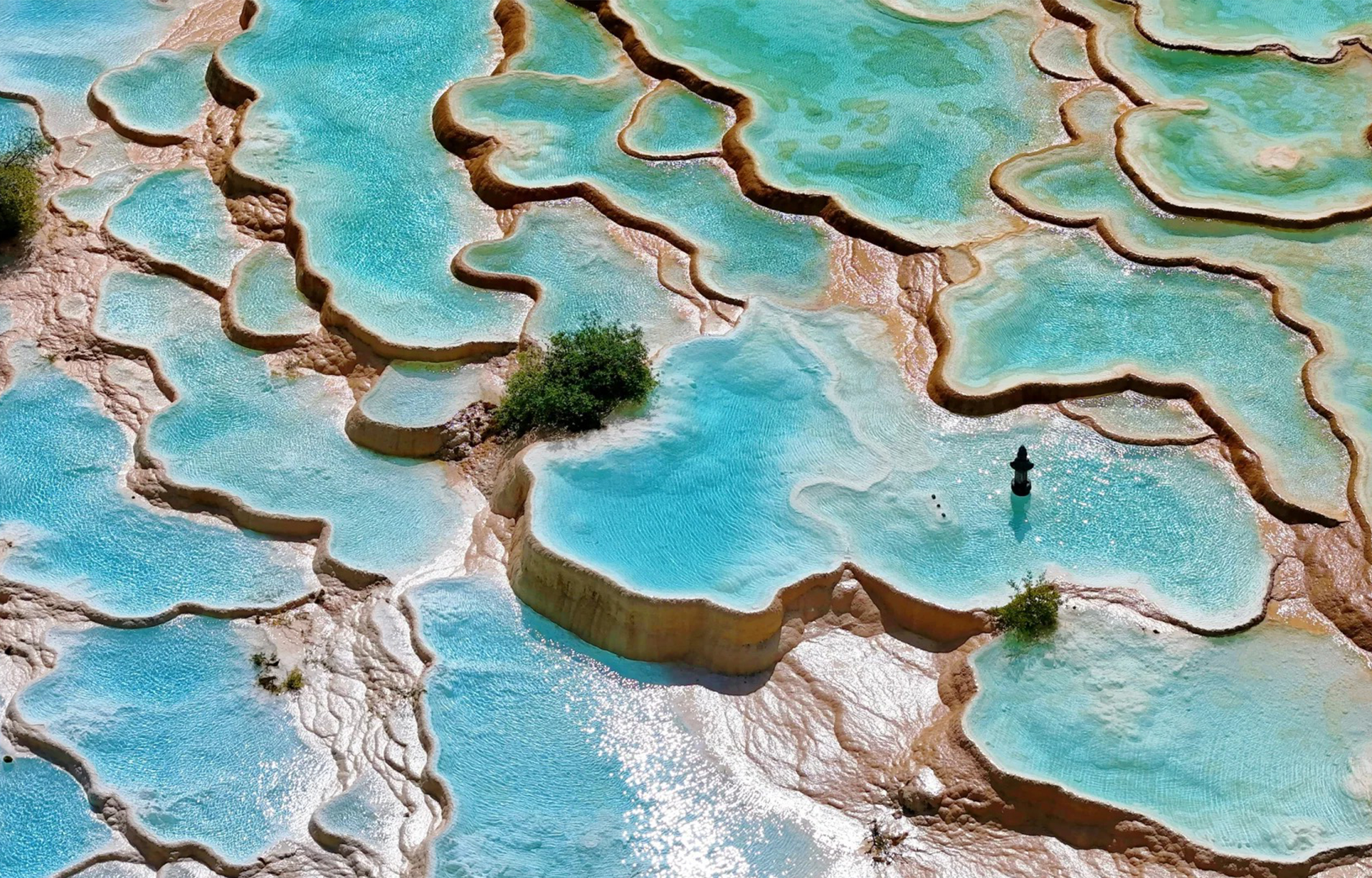 漫步在黃龍，山林間的鈣華彩池如被歲月精心雕琢的翡翠，每一道池埂都訴說著自然的神奇，彷彿踏入了夢幻秘境