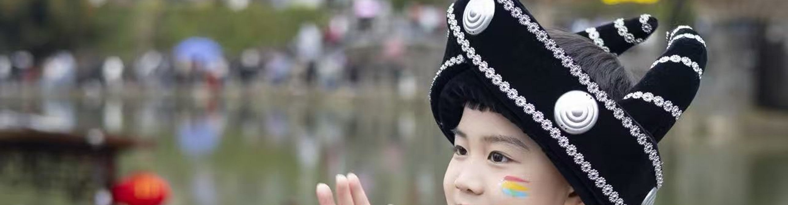 身著苗族盛裝的小男孩坐在石塊上,手撫紅面小鼓,另一隻手歡快揚起 身著苗族盛裝的小男孩坐在石塊上,手撫紅面小鼓,另一隻手歡快揚起
