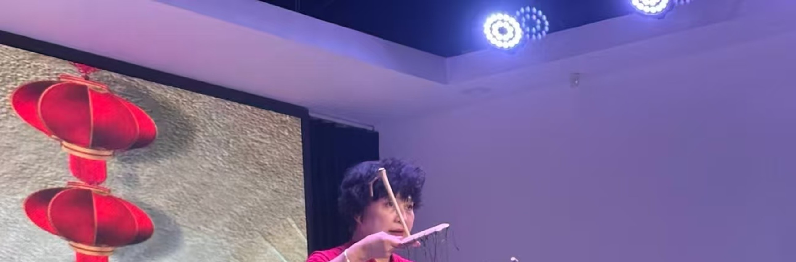 藍袍提線木偶動作活潑，手持小道具，衣飾精緻，背景是山水佈景