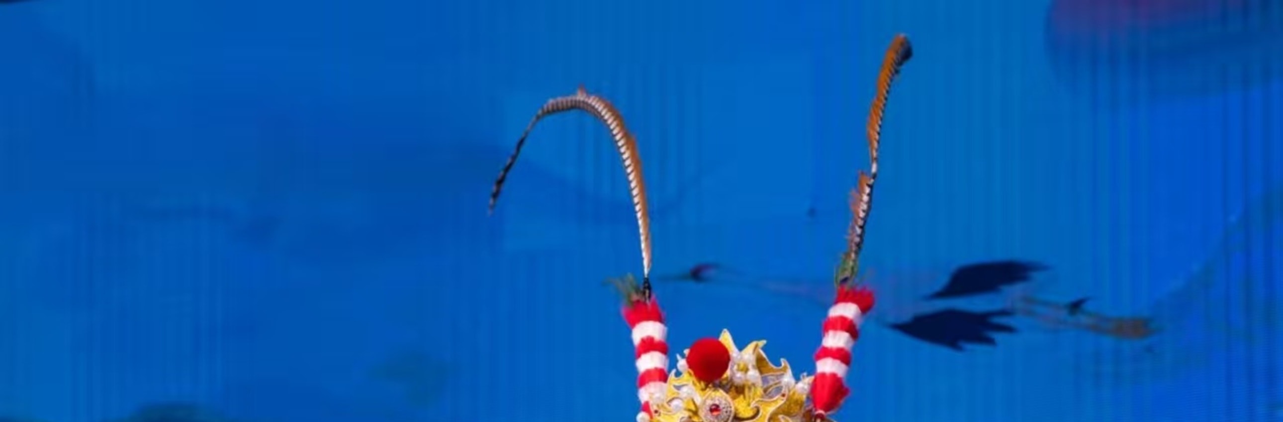 武生飾藍臉臉譜，著藍白金紋戲服，配翎子頭飾，單腿高抬展扇，旁有青衣旦角，盡顯戲曲武打的颯爽