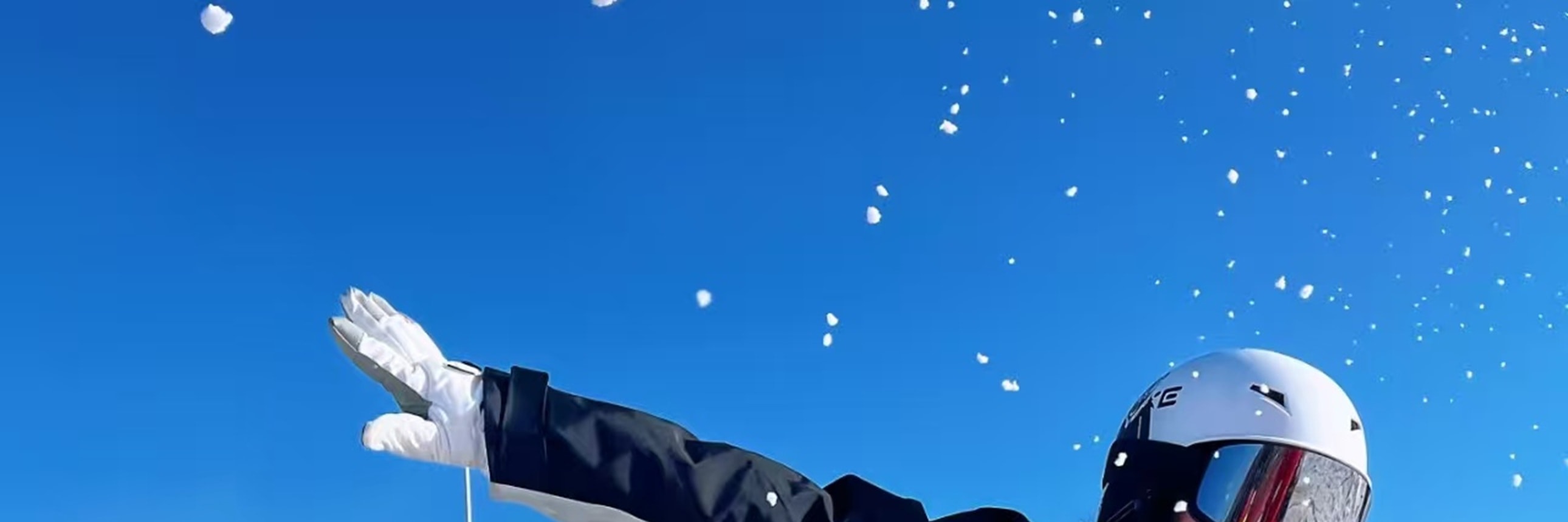 黑白裝滑雪者俯身滑行動作利落，雪粒飛濺，背景雪道人影零星，晴空下盡顯雪上運動的酷颯活力