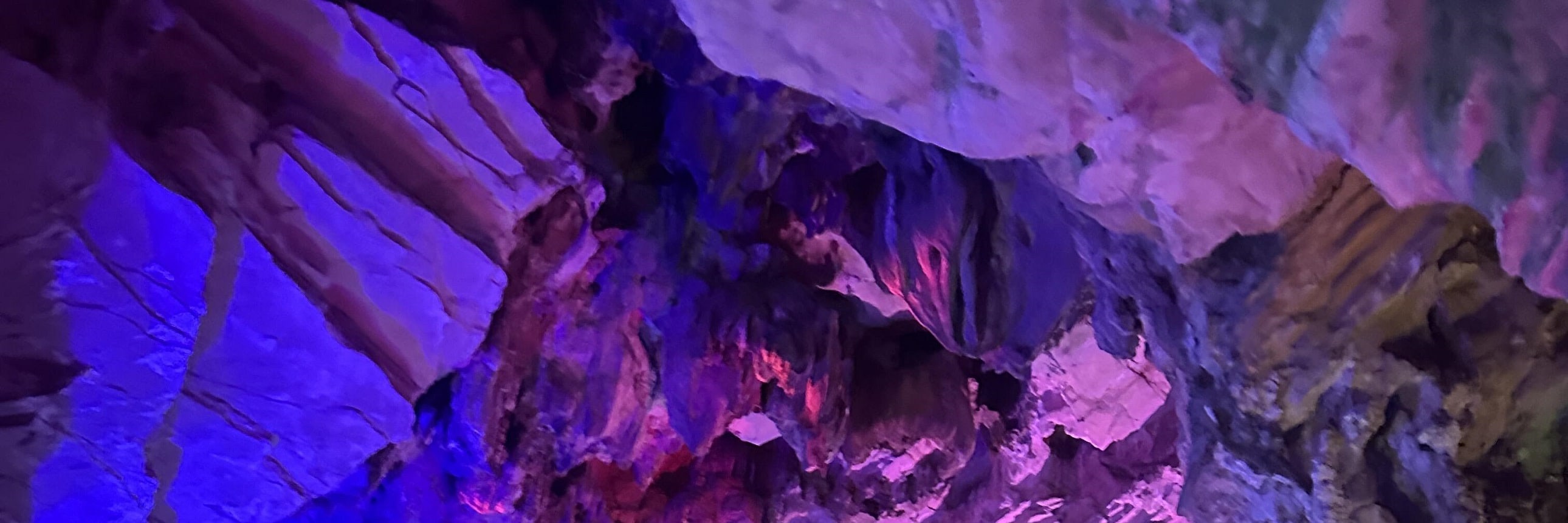 巖壁在霓虹燈光的映照下暈染出紫、粉、藍交織的奇幻色彩，鐘乳石的肌理被光影勾勒得格外生動，水面倒映著斑斕的燈光，像把整片星空都揉進了幽深的洞穴裡。彷彿闖入了地下的魔法世界，每一處光影變化都藏著大自然的鬼斧神工，神秘又絢爛，讓人挪不開眼