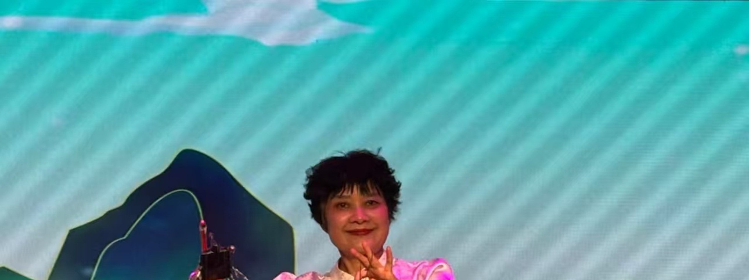 表演者操控提線木偶，木偶著黃衣紅褲挎紅籃，人偶互動生動，背景是山水橋景，盡顯傳統木偶戲的趣味