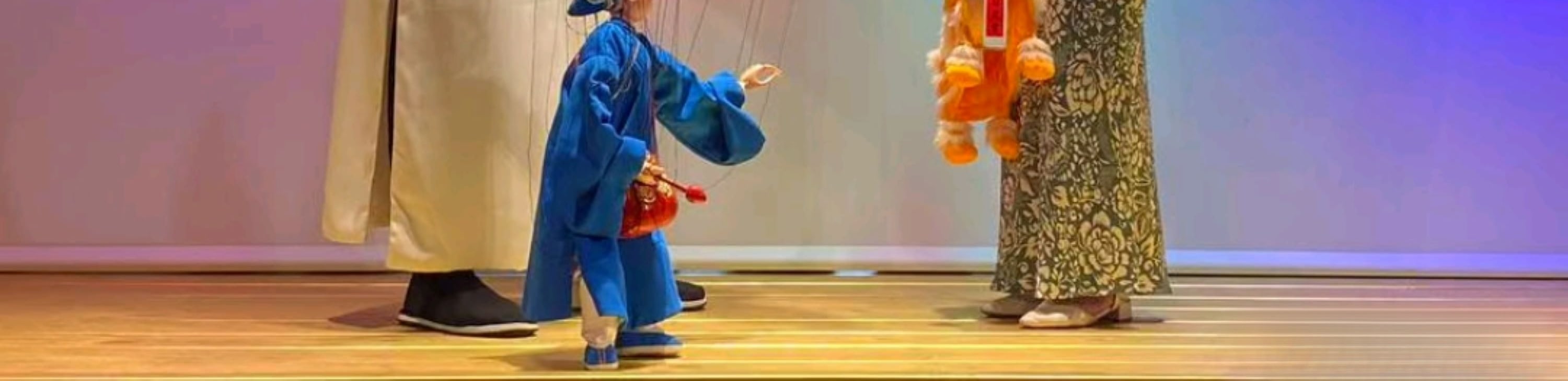 木偶戲的互動體驗場景：演員身著白色中式長衫，操控藍袍木偶