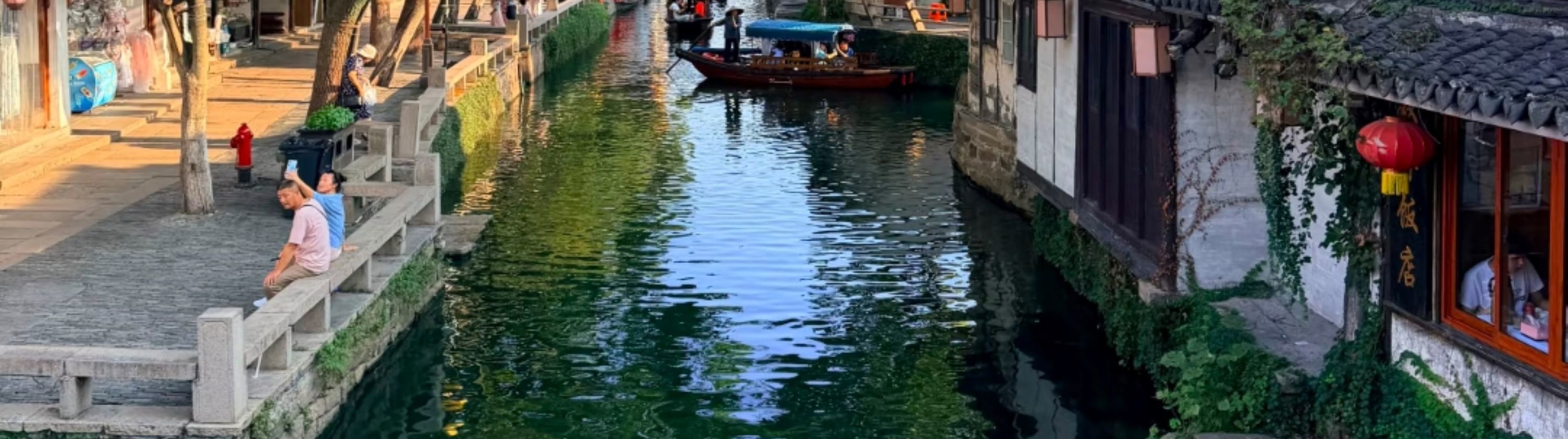周莊日間水鄉風貌,河道清澈,烏篷船悠悠穿行,兩岸黛瓦白牆的民居錯落,綠樹垂蔭,黃燈籠點綴其間,遊人或閒坐岸邊,盡顯江南古鎮的寧靜與菸火氣 周莊日間水鄉風貌,河道清澈,烏篷船悠悠穿行,兩岸黛瓦白牆的民居錯落,綠樹垂蔭,黃燈籠點綴其間,遊人或閒坐岸邊,盡顯江南古鎮的寧靜與菸火氣