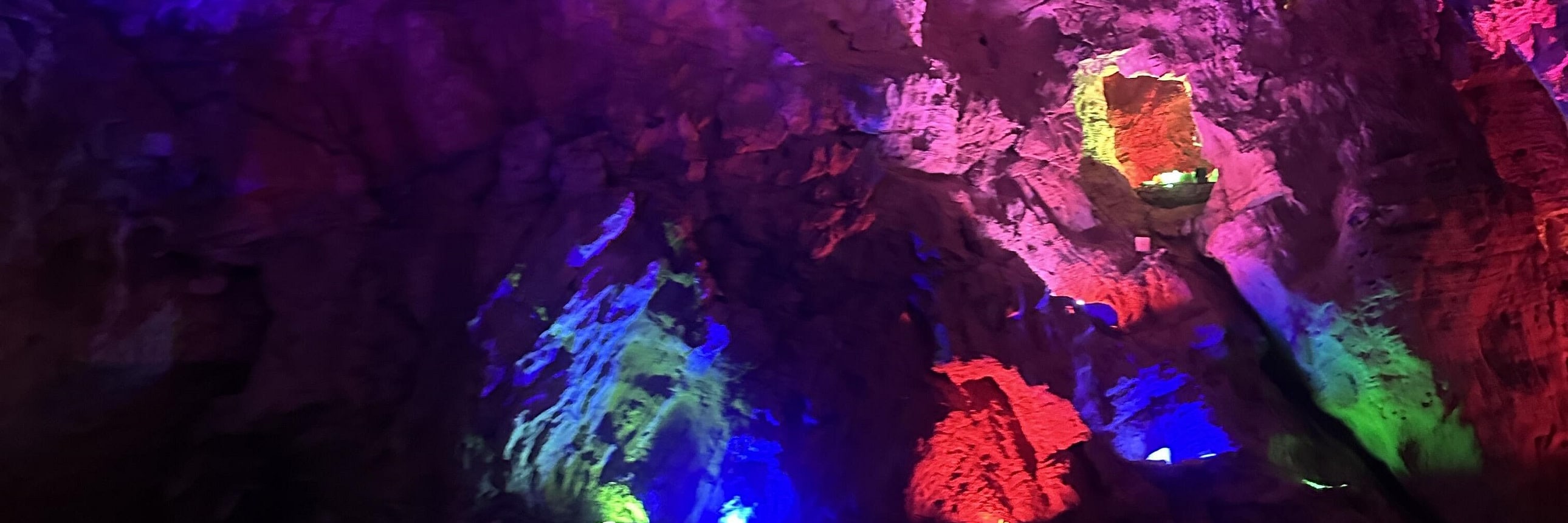 巖壁在霓虹燈光的映照下暈染出紫、粉、藍交織的奇幻色彩，鐘乳石的肌理被光影勾勒得格外生動，水面倒映著斑斕的燈光，像把整片星空都揉進了幽深的洞穴裡。彷彿闖入了地下的魔法世界，每一處光影變化都藏著大自然的鬼斧神工，神秘又絢爛，讓人挪不開眼