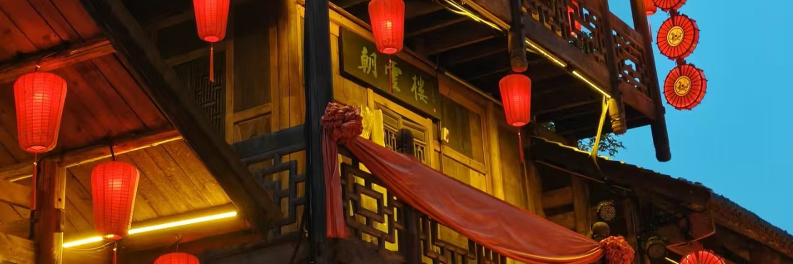 暮色漸濃時，這座三層木樓被紅燈籠與暖黃燈光點亮，層層疊疊的雕花欄杆與木樑在夜色裡格外醒目