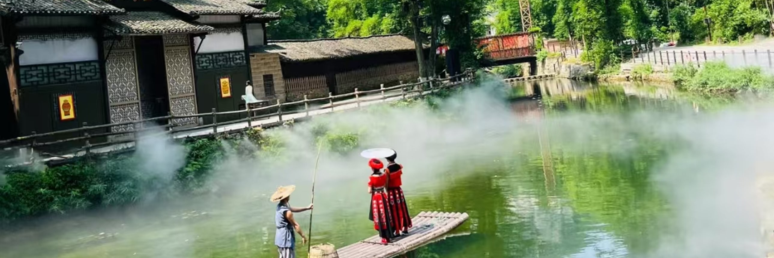 碧綠的溪面上，一葉竹筏輕搖，撐筏人戴著斗笠，兩位身著紅裙、頭戴斗笠的女子立於筏上