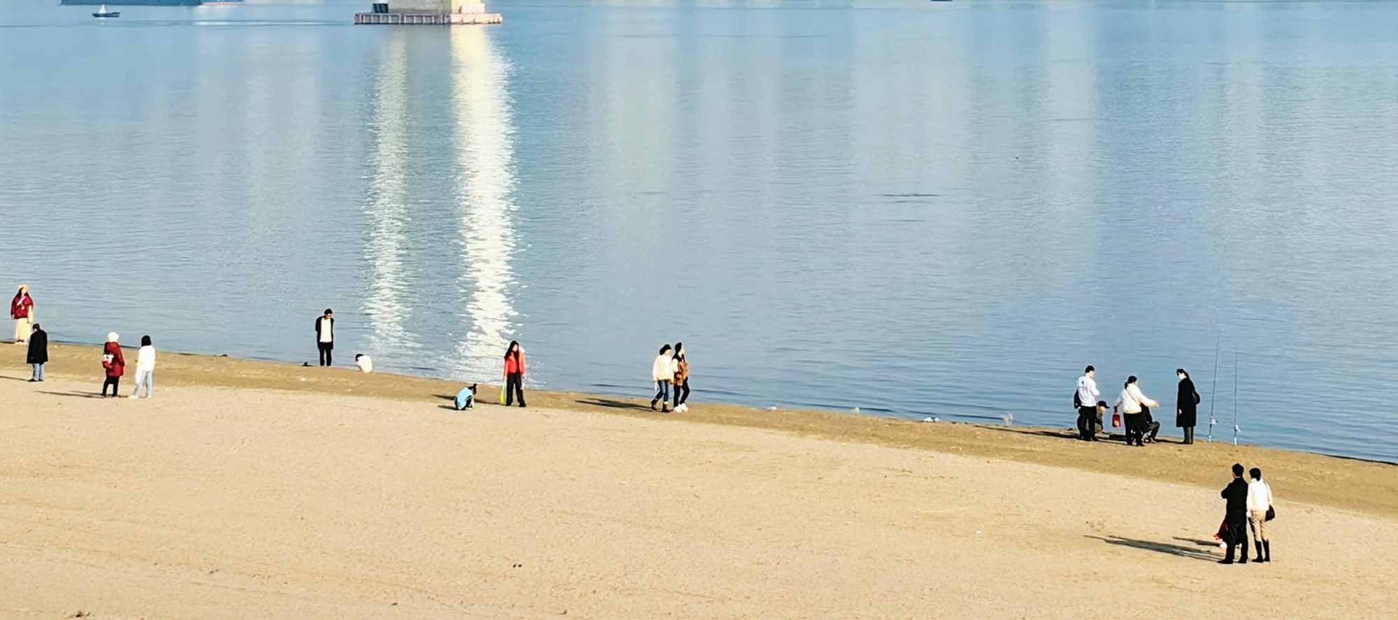 漢口江灘，白沙碧水間，大橋橫跨如虹。遊人漫步嬉戲，繪就江城閒適生活畫卷