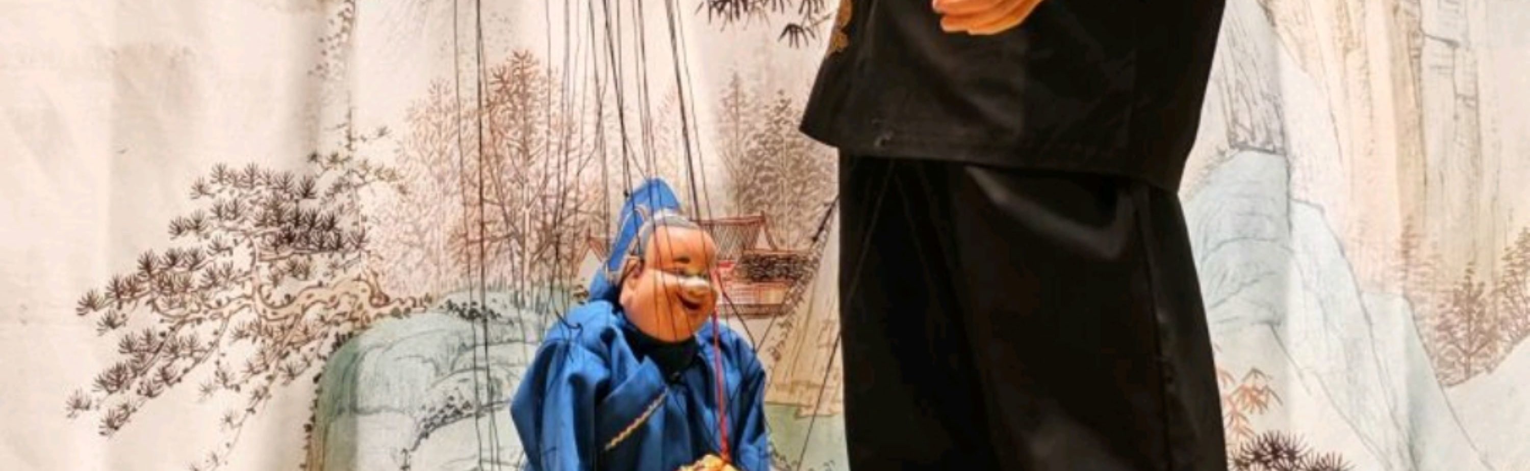 演員操控藍袍提線木偶，木偶挎紅飾道具，盡顯木偶戲的傳統美學