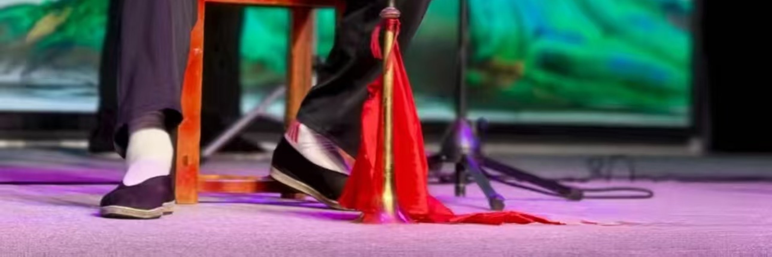 樂師持板胡演奏，著淺白衣褲，背景是青綠山水屏，神情投入，盡顯傳統樂器演奏的專注與韻味