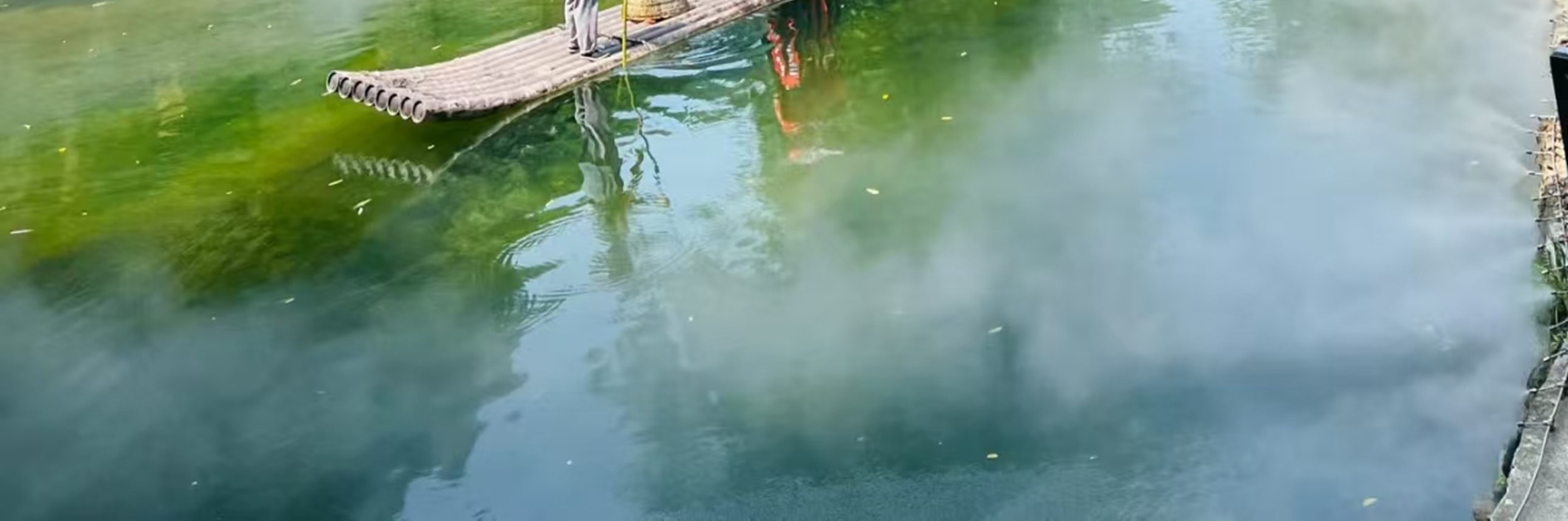 碧綠的溪面上，一葉竹筏輕搖，撐筏人戴著斗笠，兩位身著紅裙、頭戴斗笠的女子立於筏上