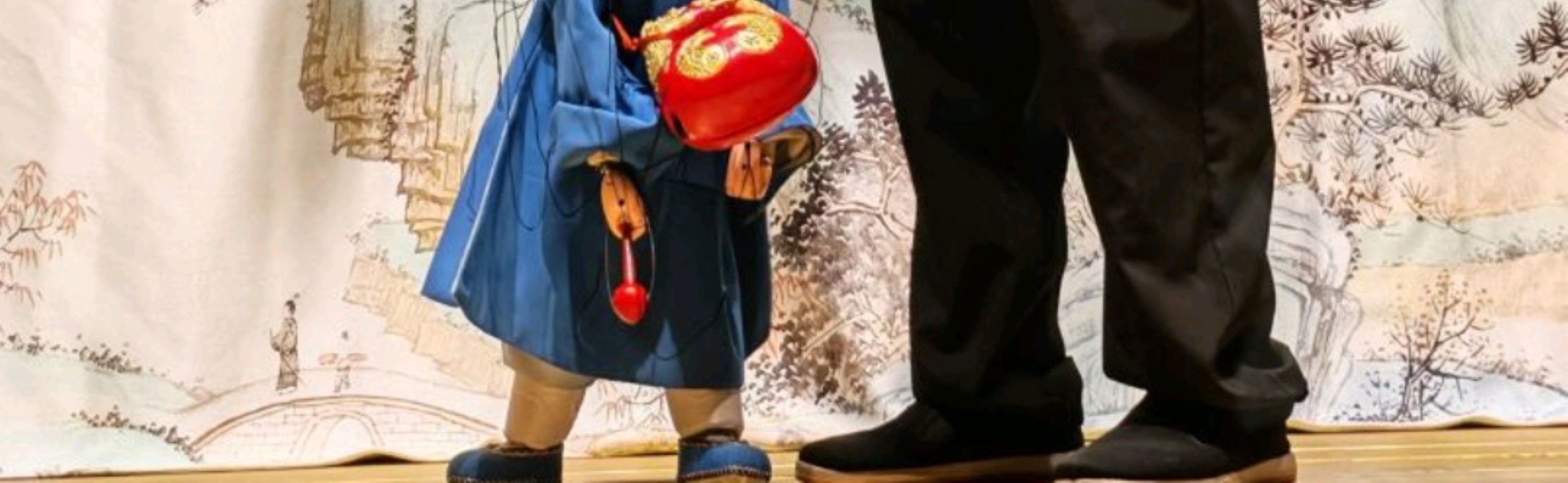 演員操控藍袍提線木偶，木偶挎紅飾道具，盡顯木偶戲的傳統美學