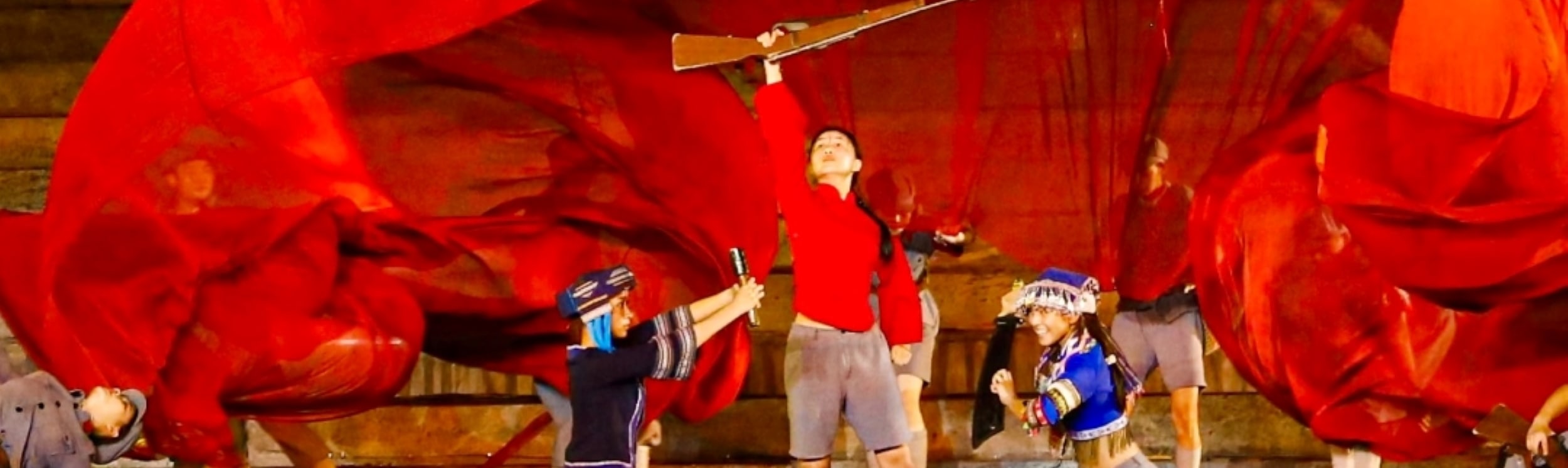 紅綢幕布裹戰場，演員持槍躍起，以動感姿態繪娘子軍戰鬥豪情