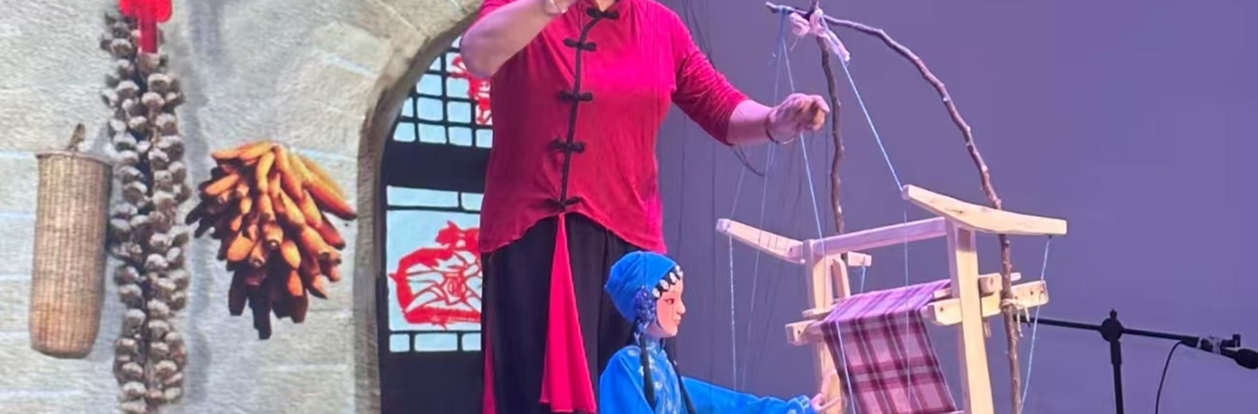 藍袍提線木偶動作活潑，手持小道具，衣飾精緻，背景是山水佈景