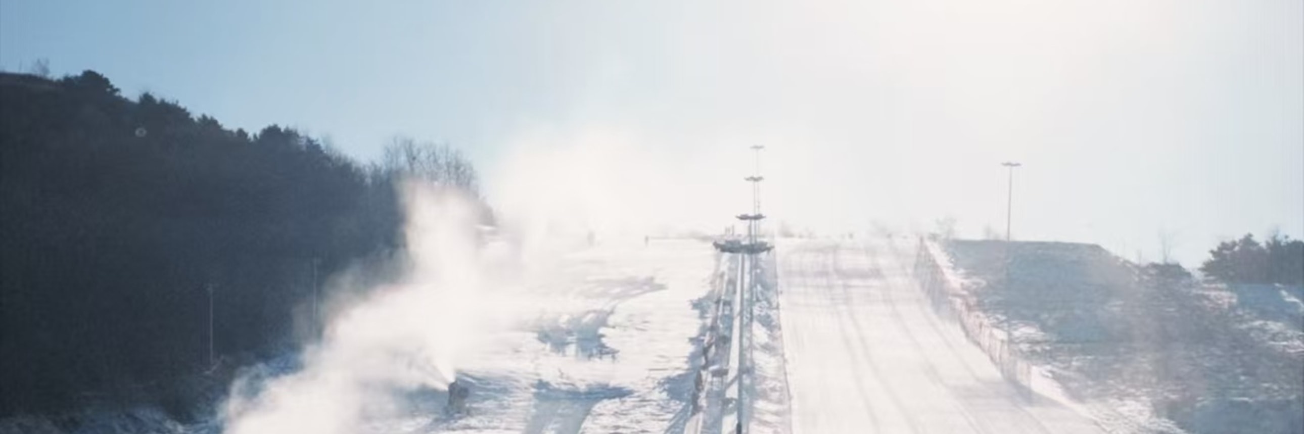 從雪坡頂俯瞰，雪場建築與人群清晰，遠山藏著塔影，近景雪具閒置，開闊視野裹著雪場的熱鬧菸火