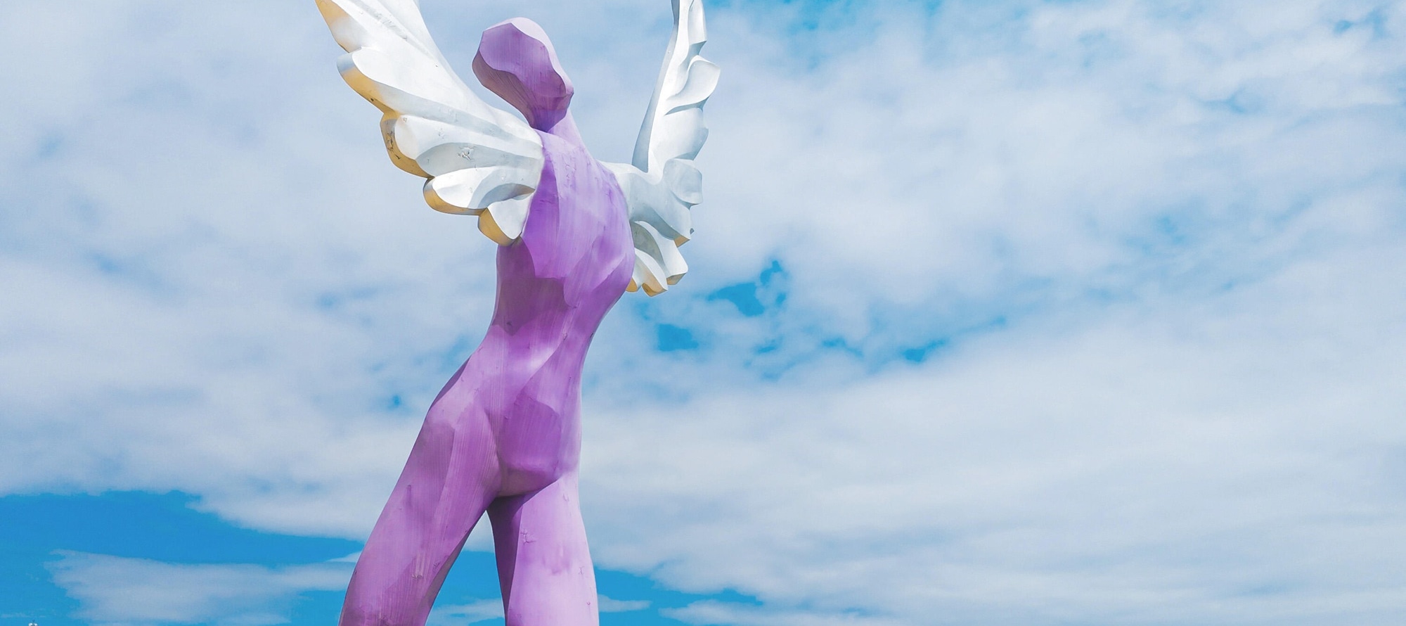 The Dameisha Wing Sculpture, with its purple body and white feathers, stands on the golden beach, painting a free and romantic seaside scene with the sea and sky.