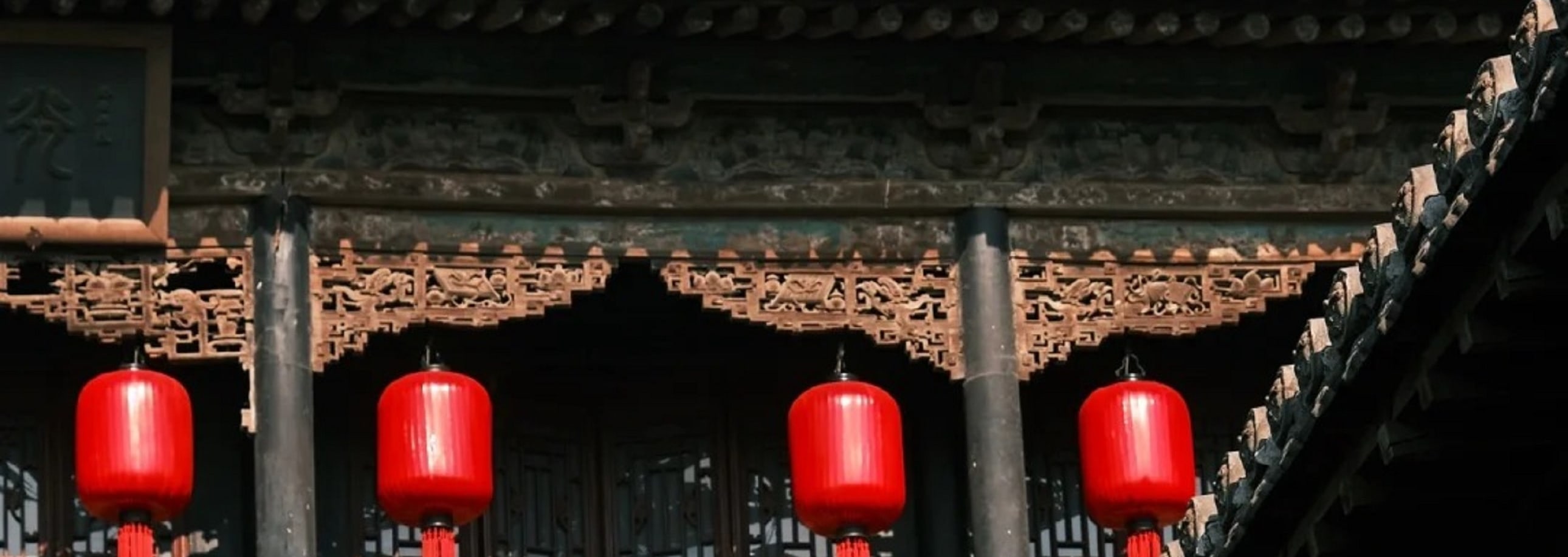 古建屋簷下紅燈籠高掛，雕樑畫棟細節精緻，紅灰色調交織，盡顯中式古建築的典雅韻味與傳統風情