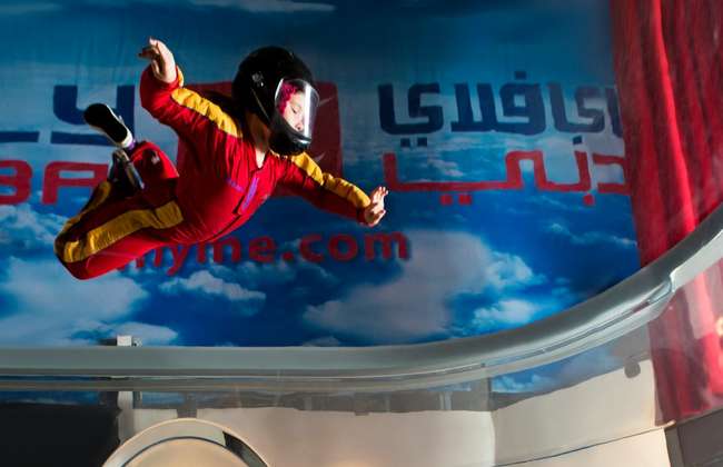 A participant in a red flight suit floats inside the iFly Dubai indoor wind tunnel.