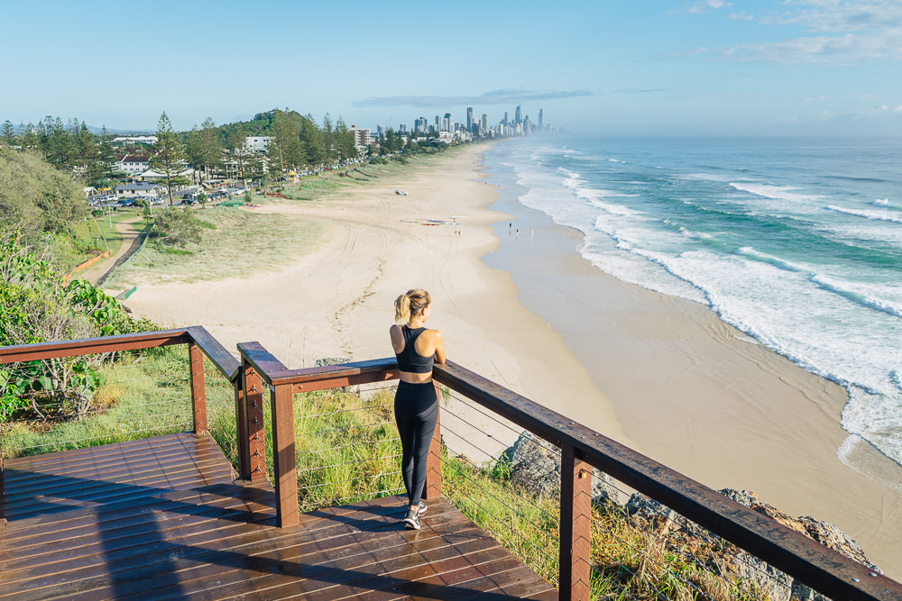 A woman, back facing the camera, standing on the Mick Schamburg Park Lookout, and looking at the beach