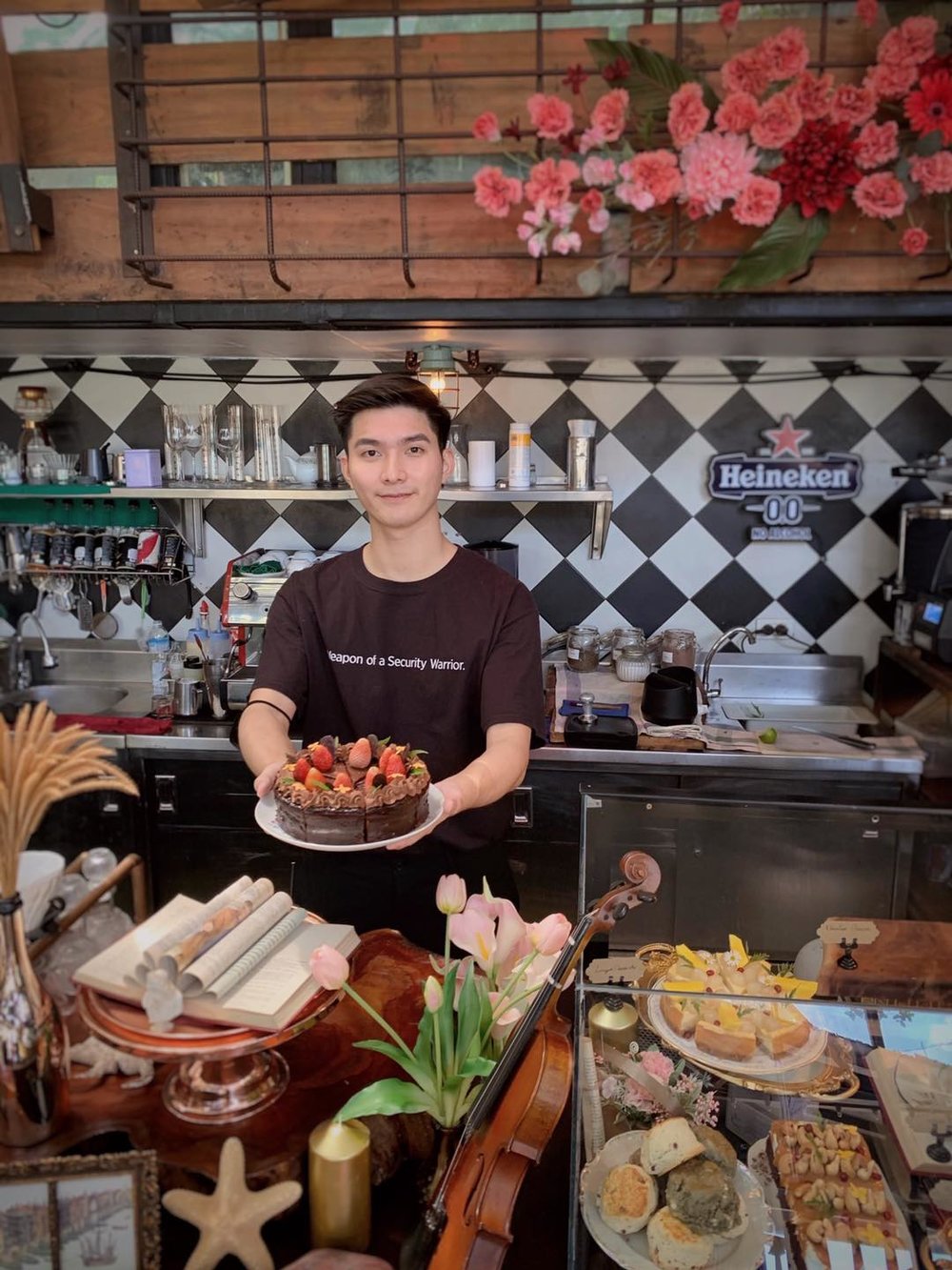 asian guy holding a chocolate cake inside a cafe