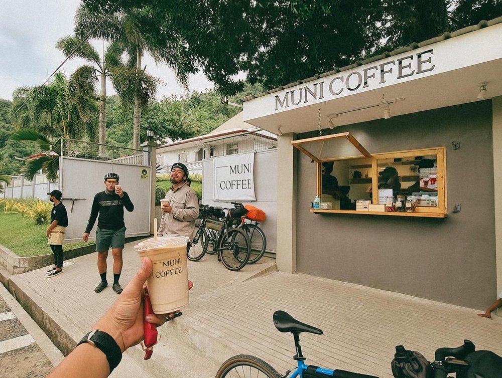 two cyclists holding cup of coffee by muni coffee cafe in laguna